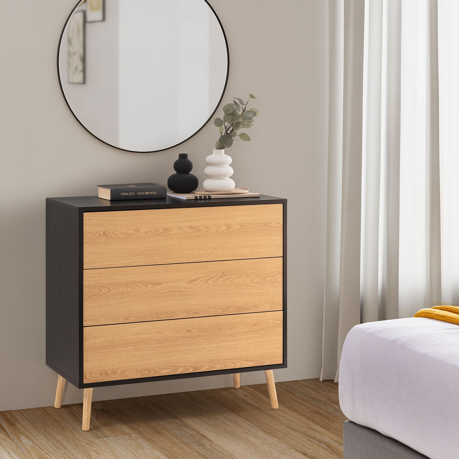 Cómoda de tres cajones de madera junto a una cama, espejo y cortinas.