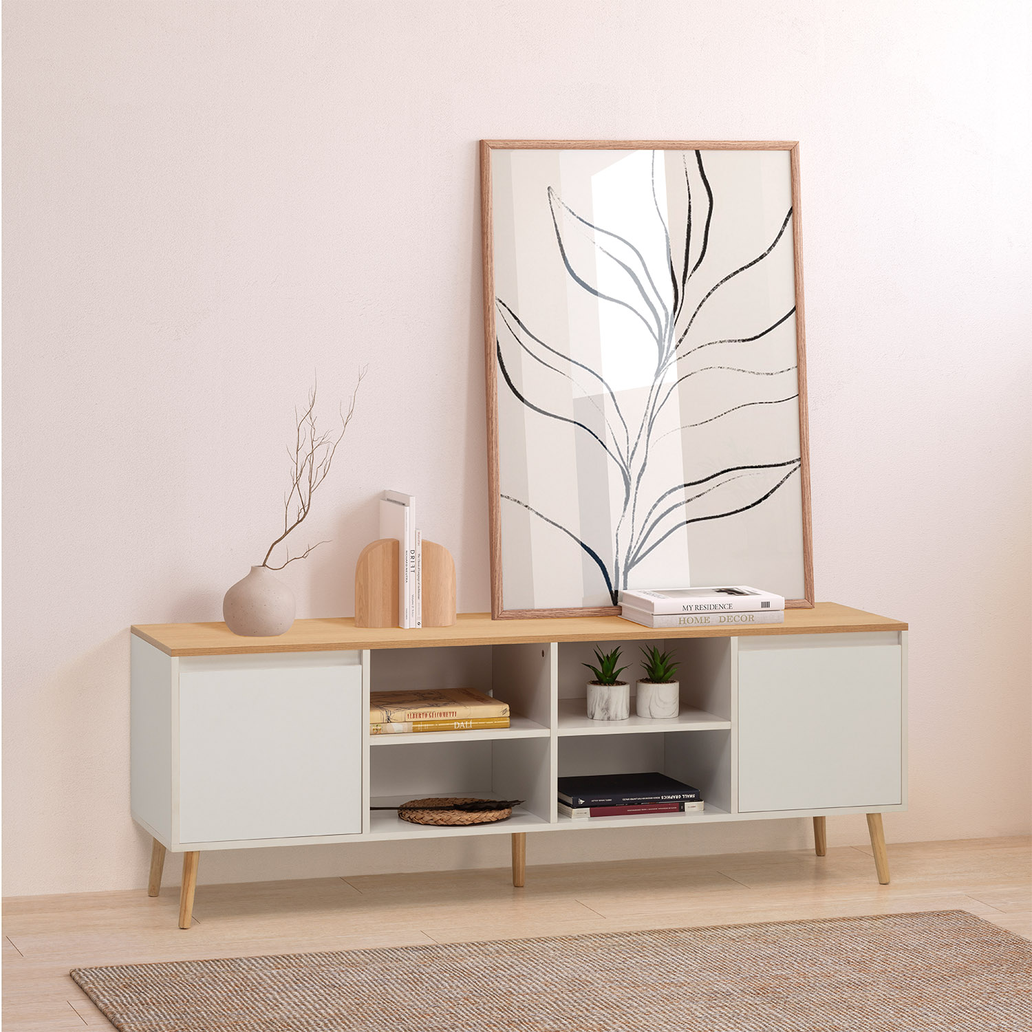 Un mueble de TV blanco con tapa de madera, libros, plantas y lámina de hojas.