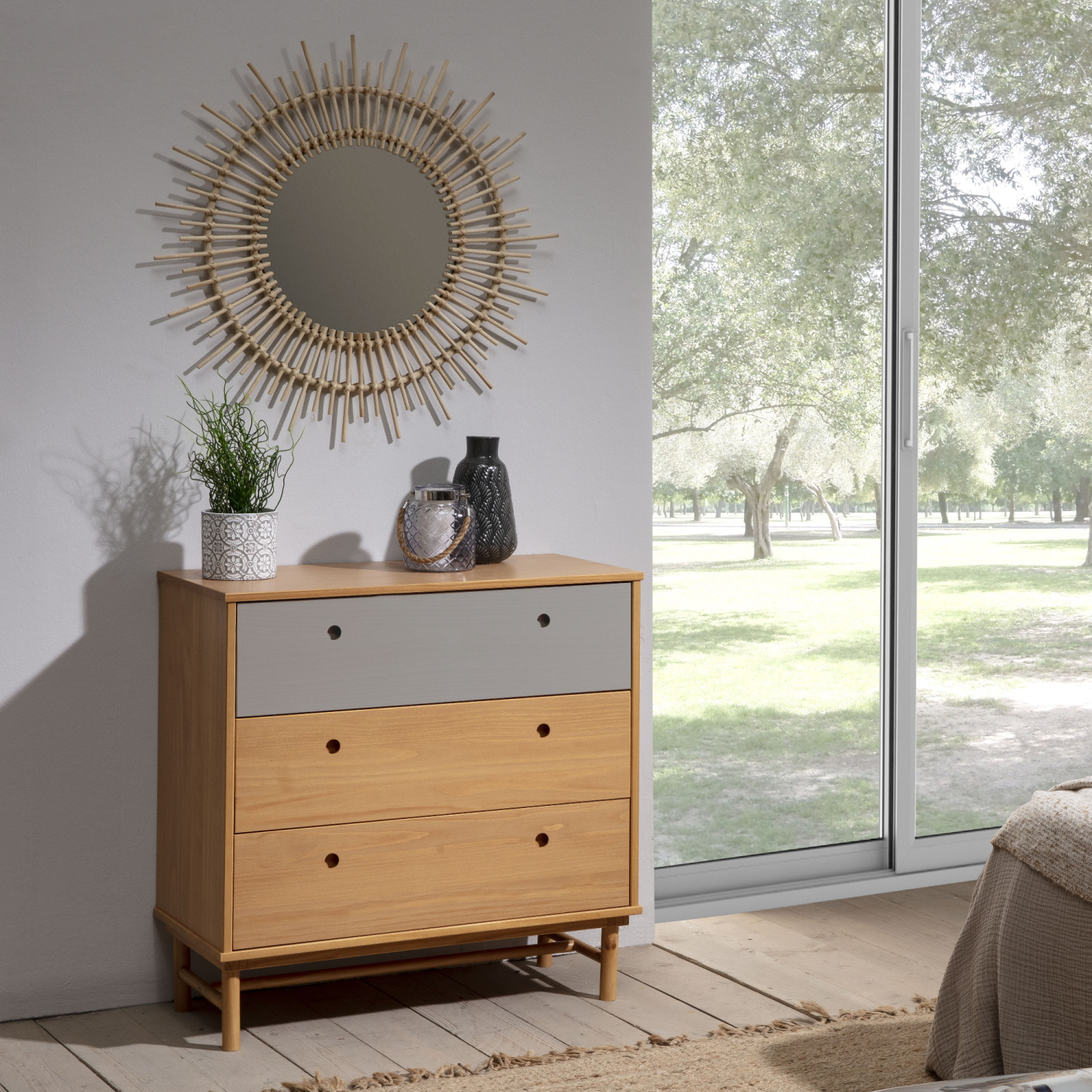 Cómoda de madera con tres cajones junto a una ventana con vistas a árboles.