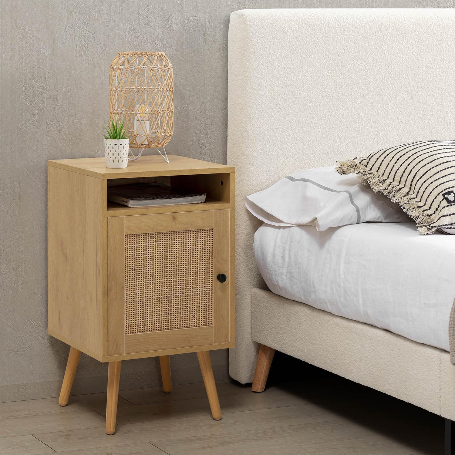 Mesita de noche de madera con puerta de ratán junto a una cama con sábanas blancas.