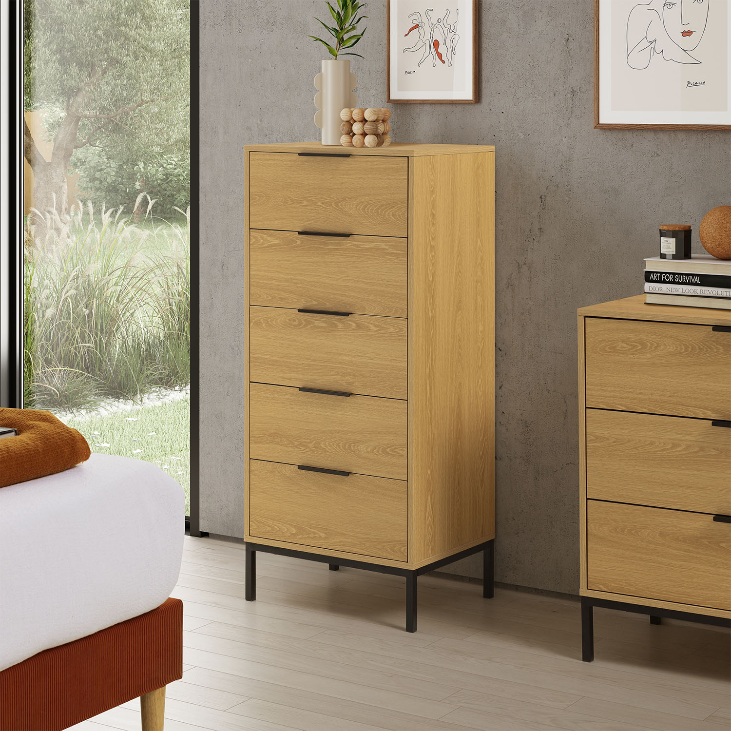 Una cómoda de madera clara con tiradores negros se alza junto a una cama y una ventana.