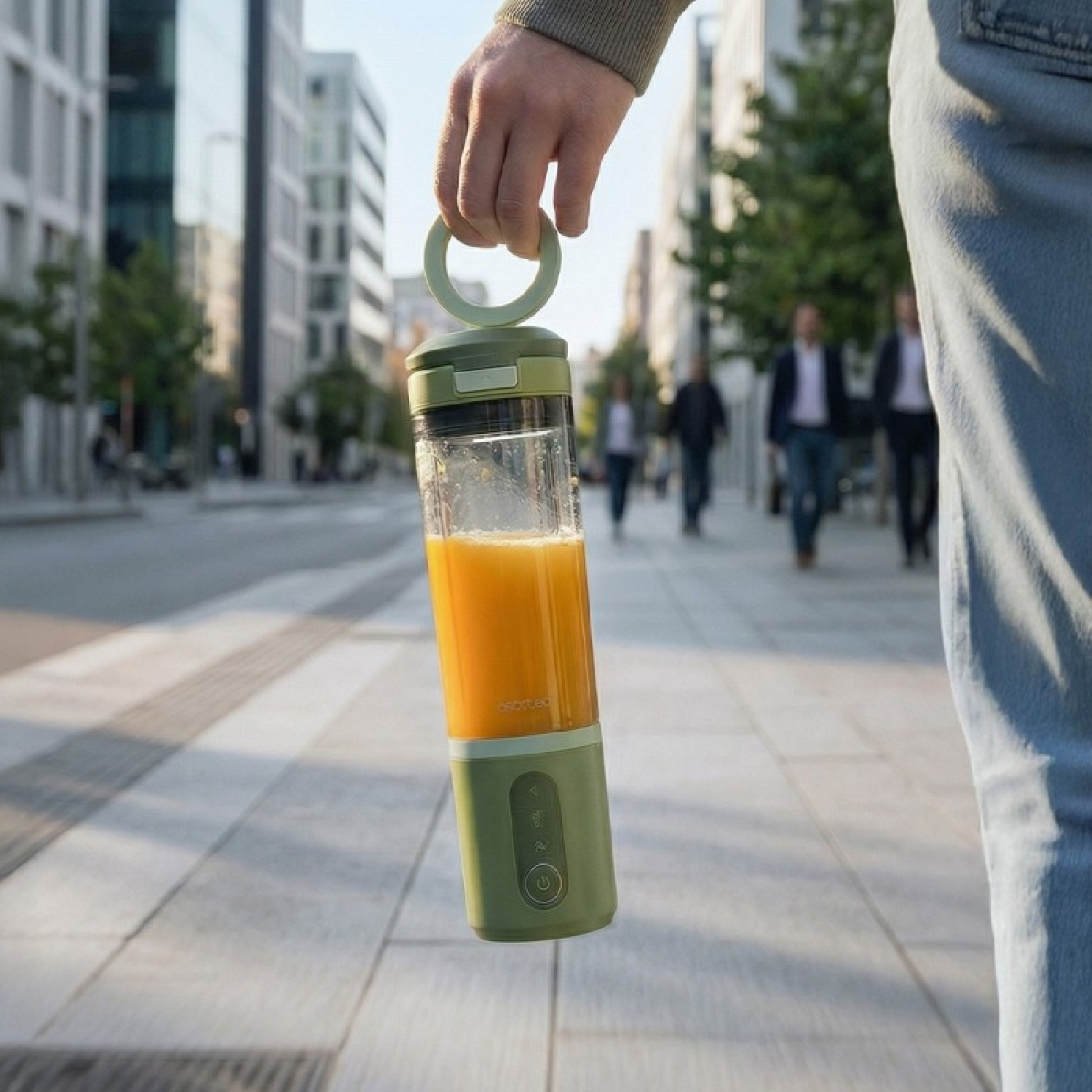 Batidora verde con jugo de naranja en la mano, fondo de ciudad.