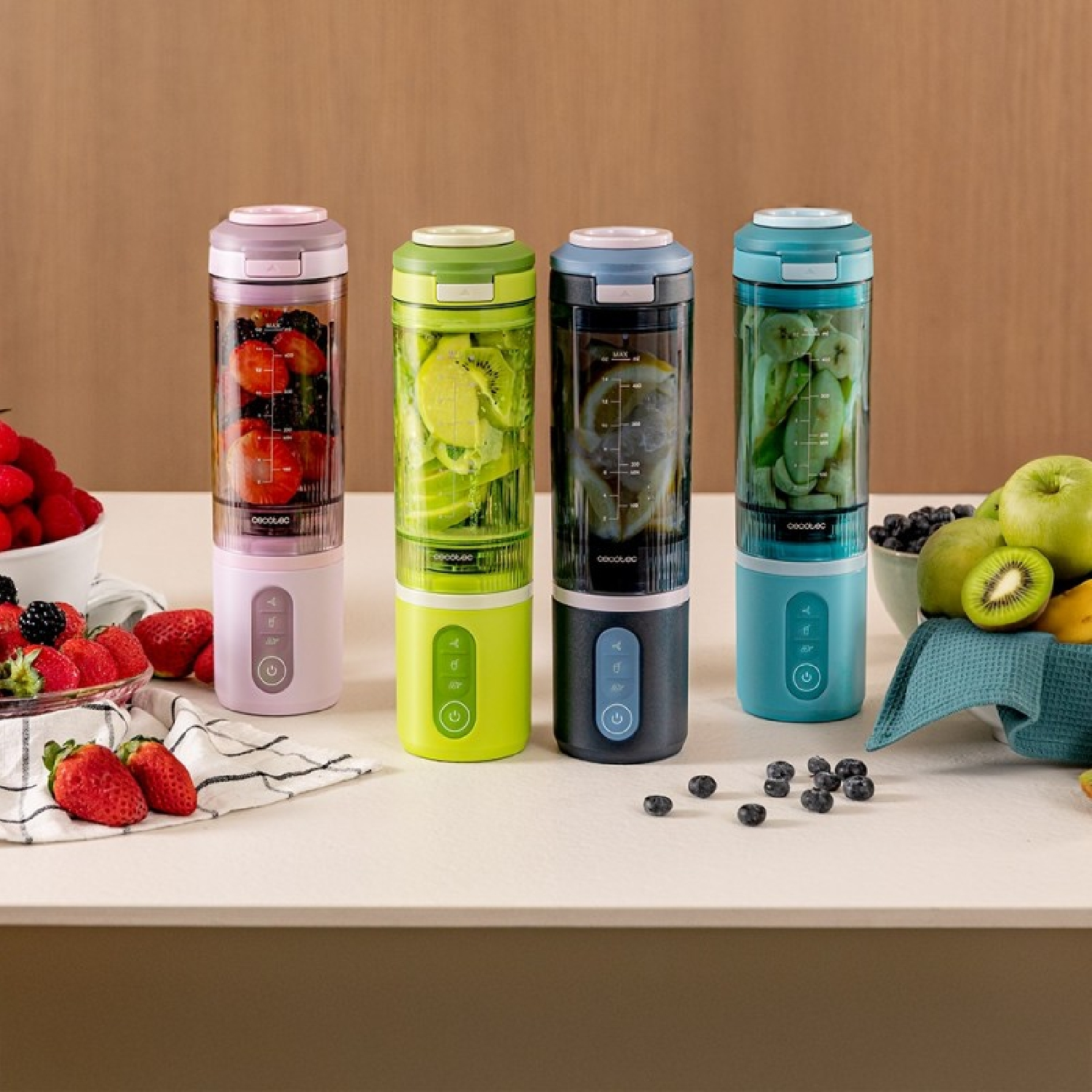 Cuatro licuadoras portátiles con fruta: rosa con fresas, verde con kiwi, negra con limón, azul con plátano.