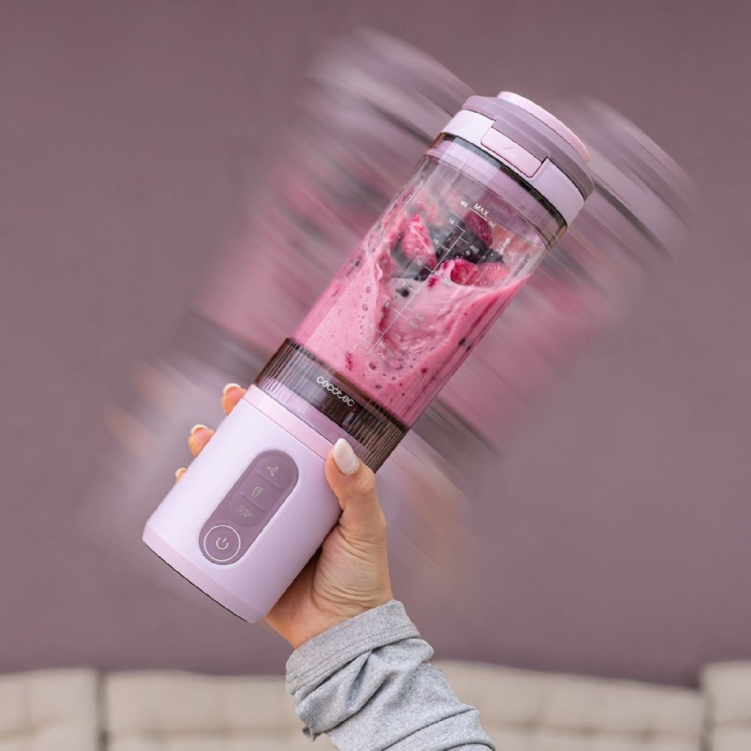 Una mano sostiene una licuadora portátil con un batido rosa y bayas dentro.