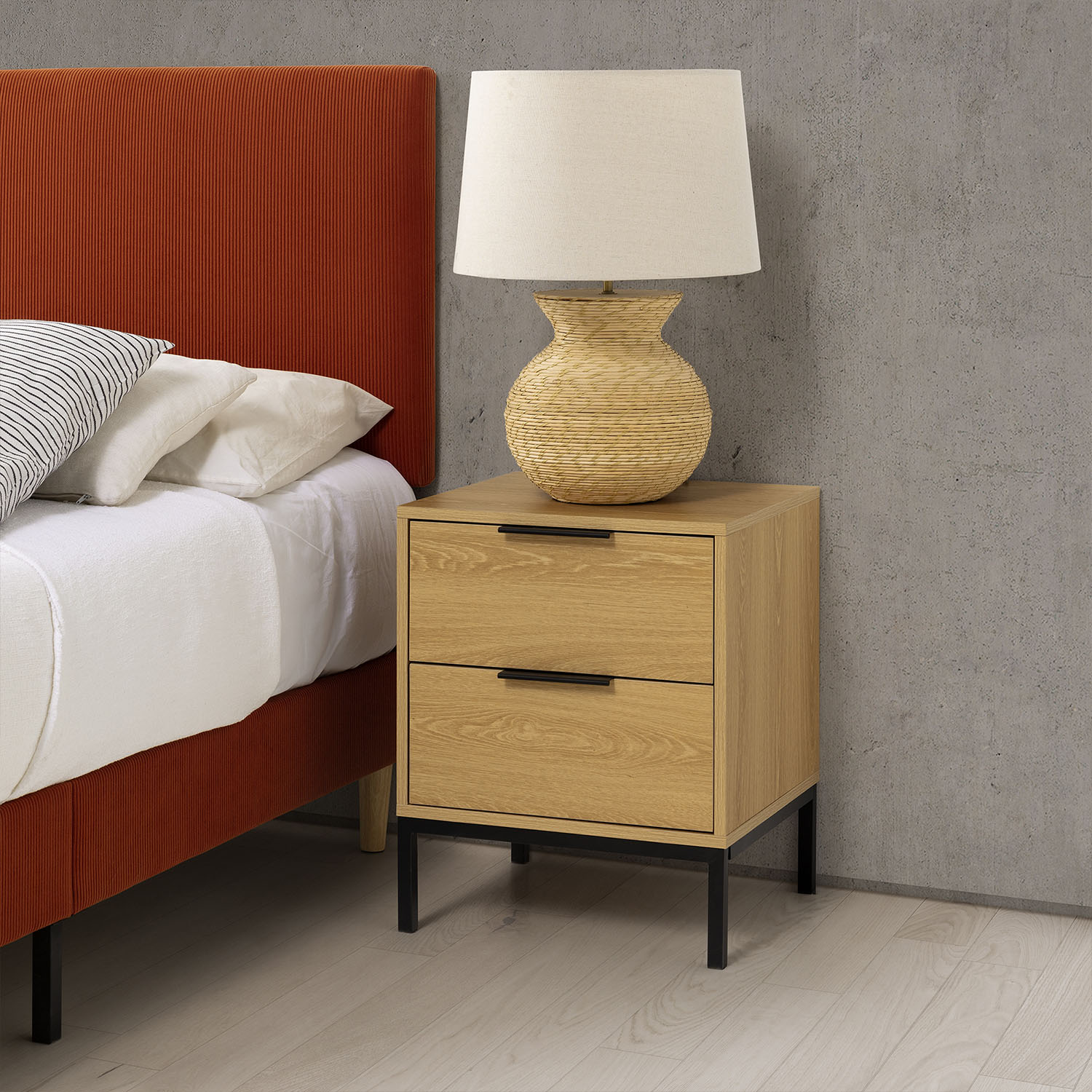 Una mesita de noche de madera con dos cajones junto a una cama con cabecero naranja.