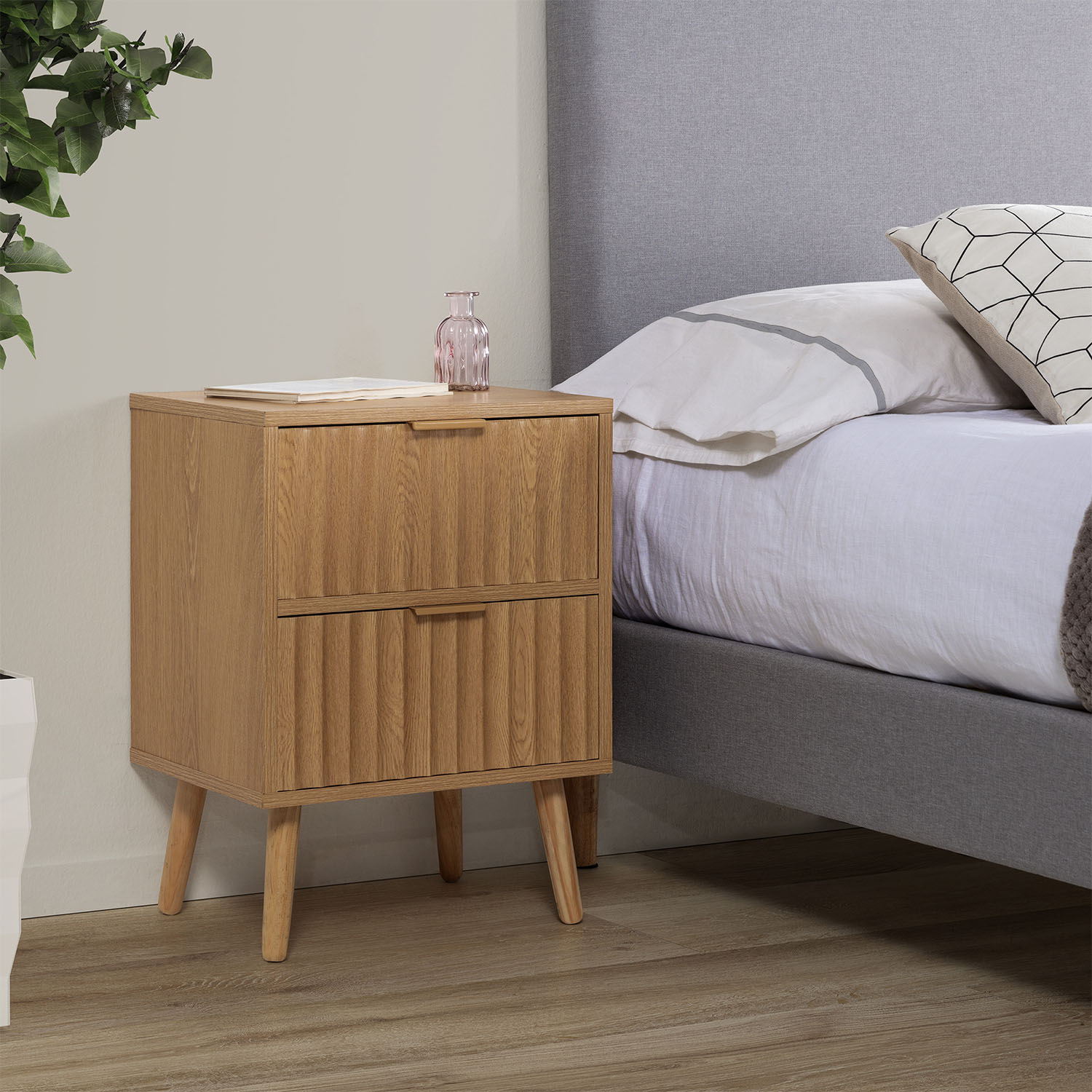 Mesita de noche de madera junto a una cama con cabecero gris y cojines.