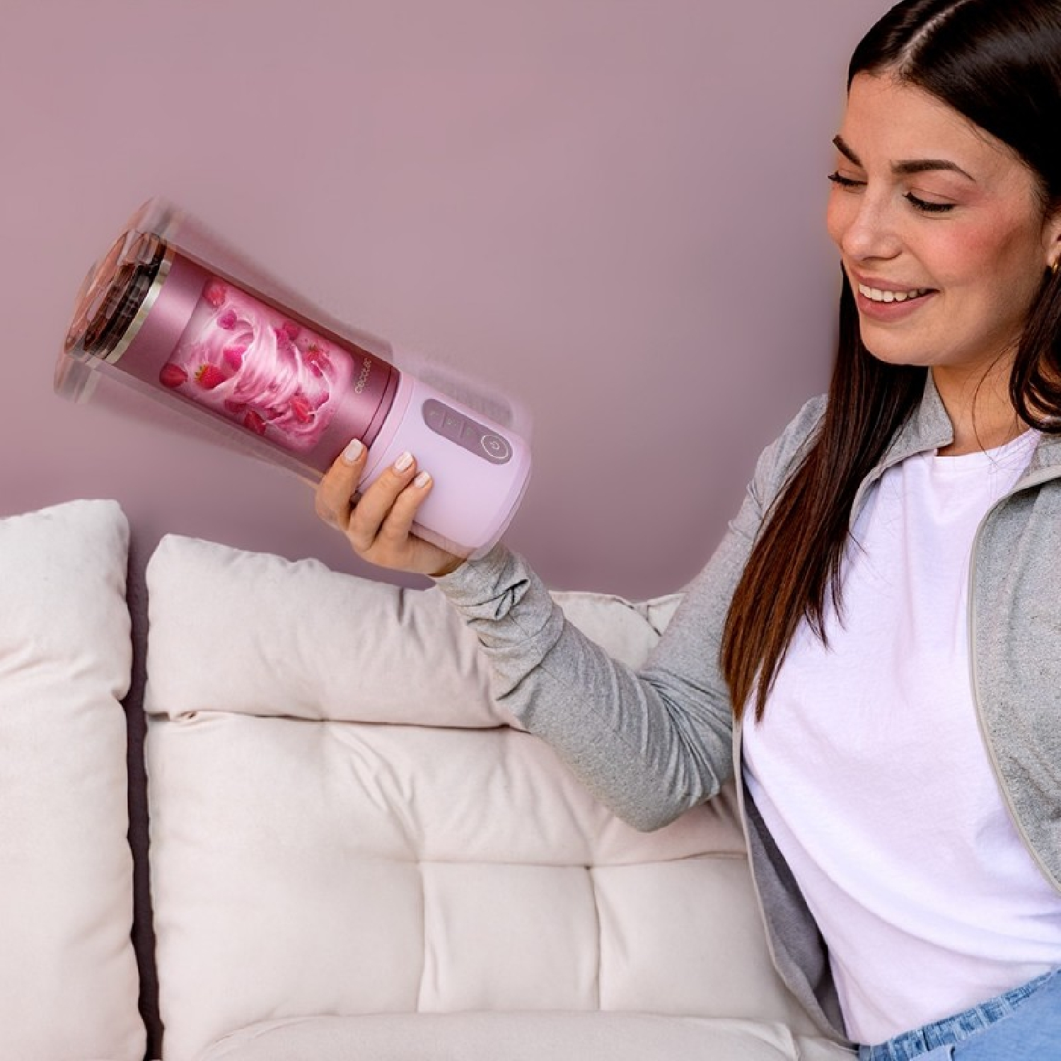 Una mujer sostiene una licuadora rosa con fresas y crema. Ella sonríe.
