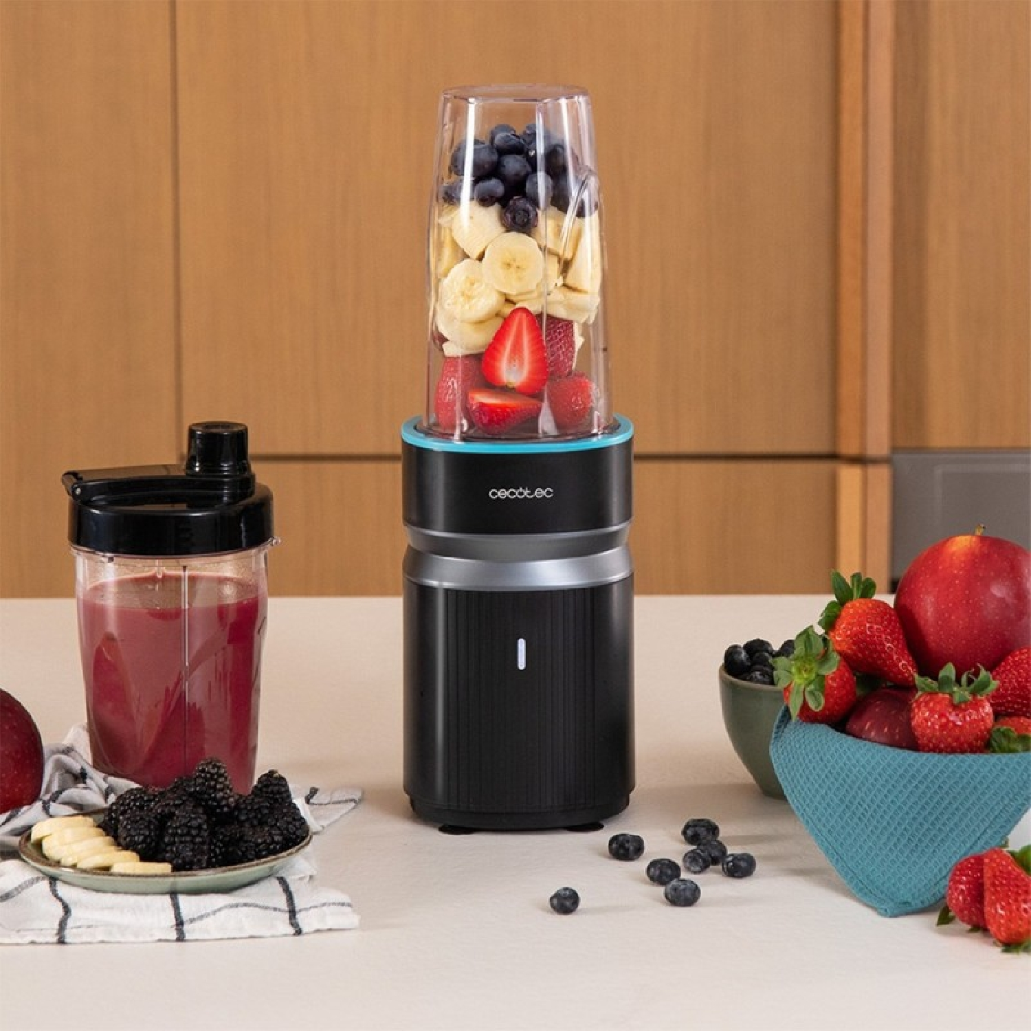 Un frullatore per frullati con frutta e bacche nel suo contenitore. Un frullato pronto è nelle vicinanze.