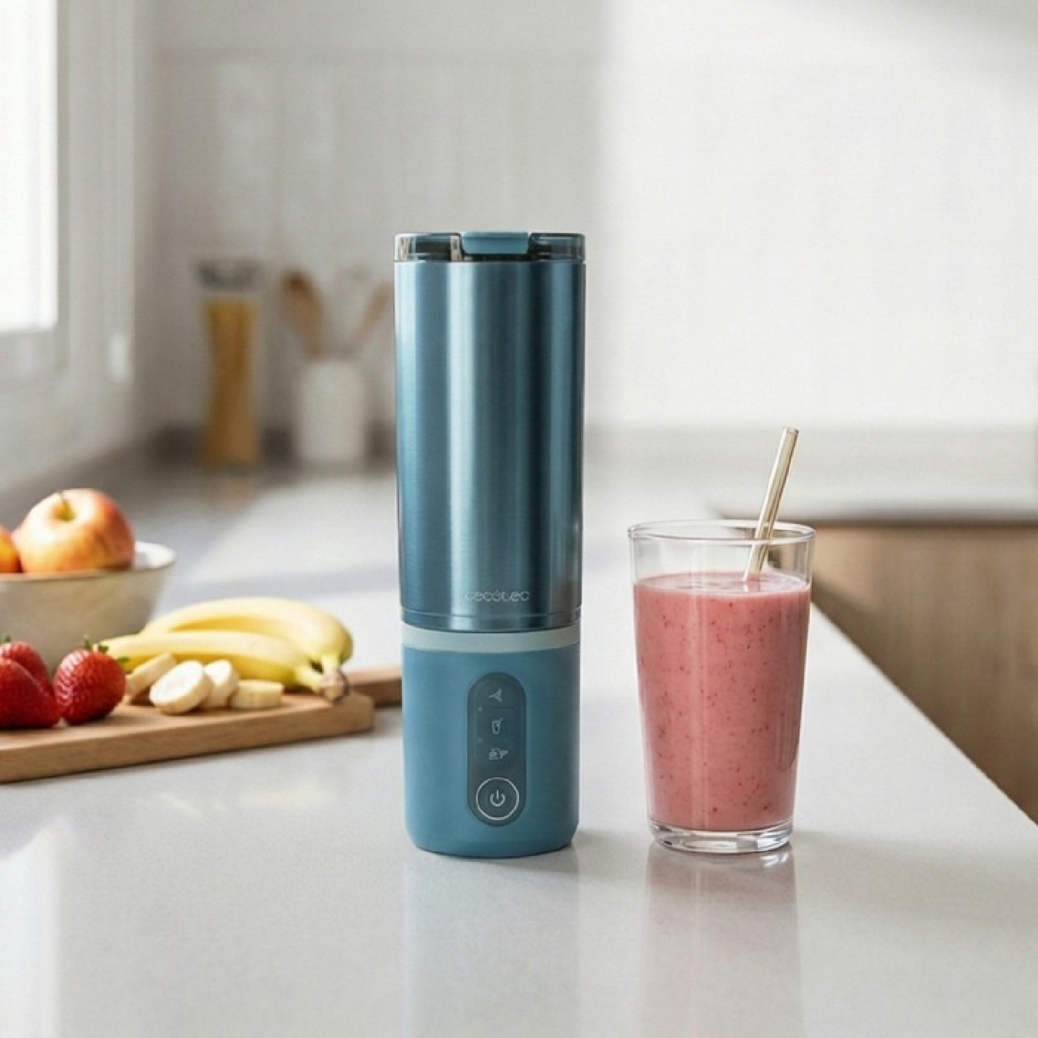 Una licuadora azul junto a un vaso de batido de fresa y plátano.