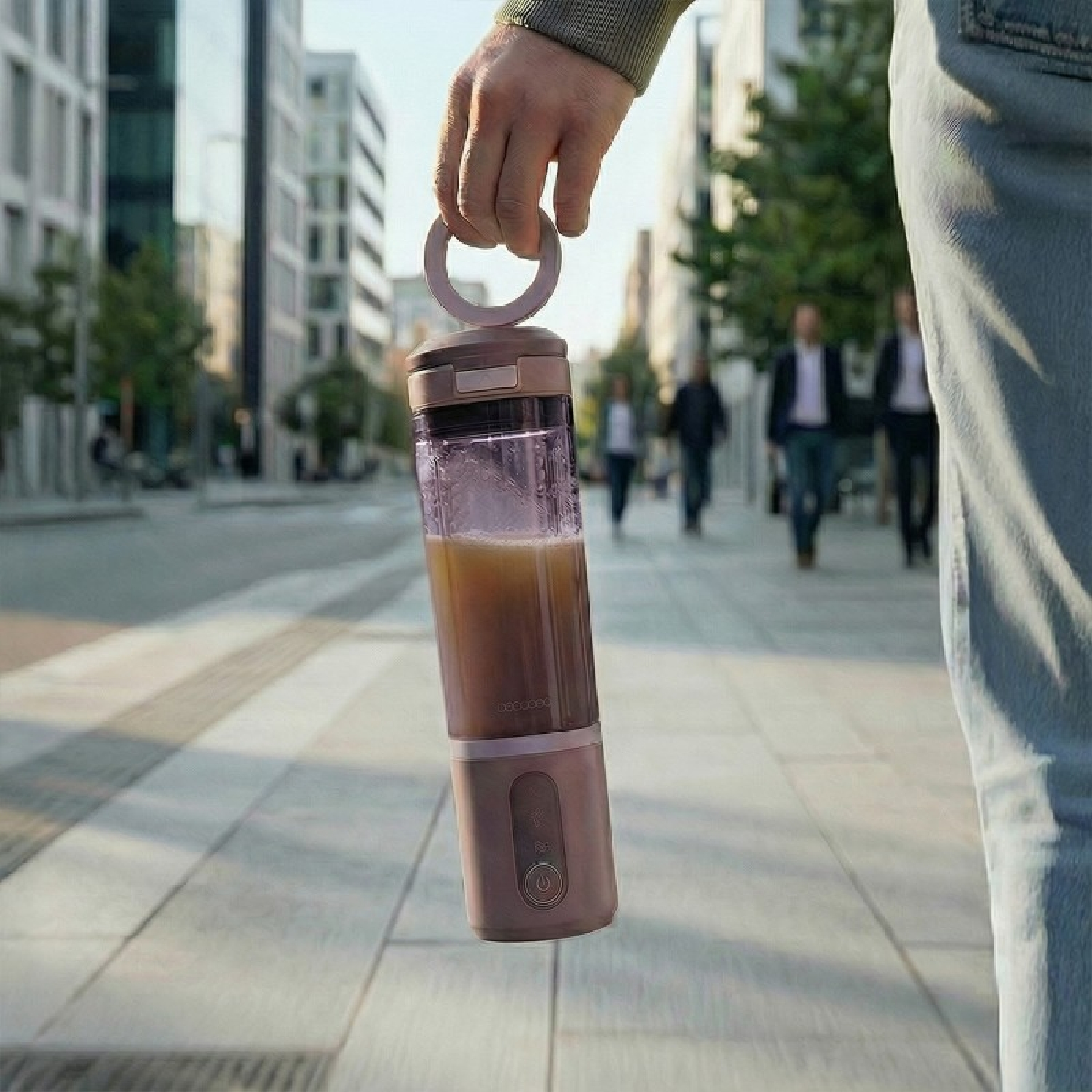 Una mano sostiene una licuadora portátil con contenido marrón en una calle de la ciudad.