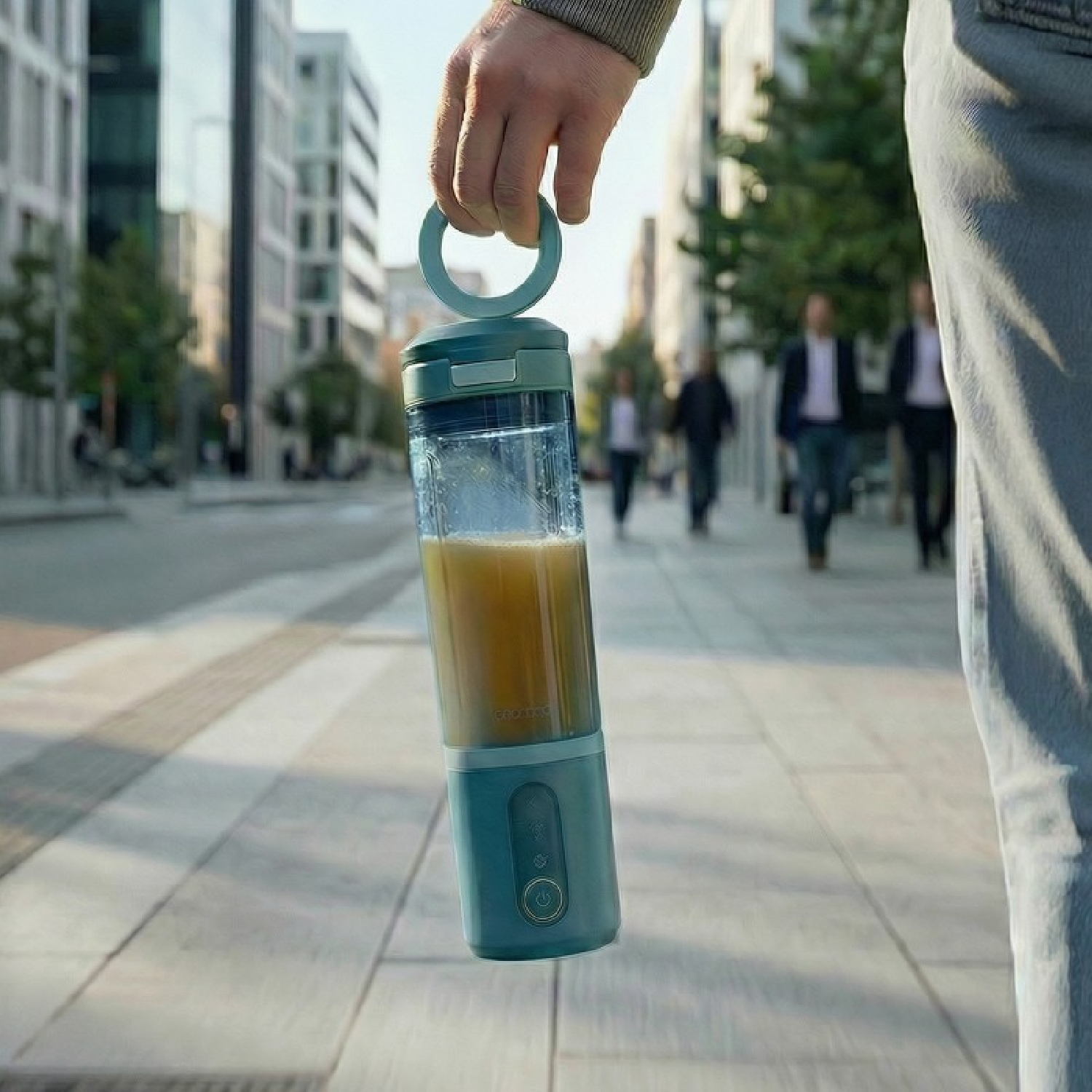 Una persona sostiene una batidora portátil turquesa con jugo. Fondo de calle.
