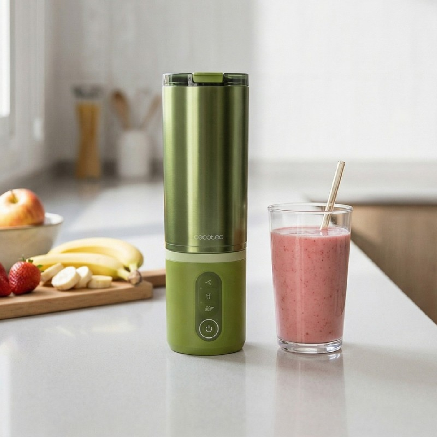 Una licuadora verde junto a un vaso de batido con fresas y plátanos sobre la mesa.
