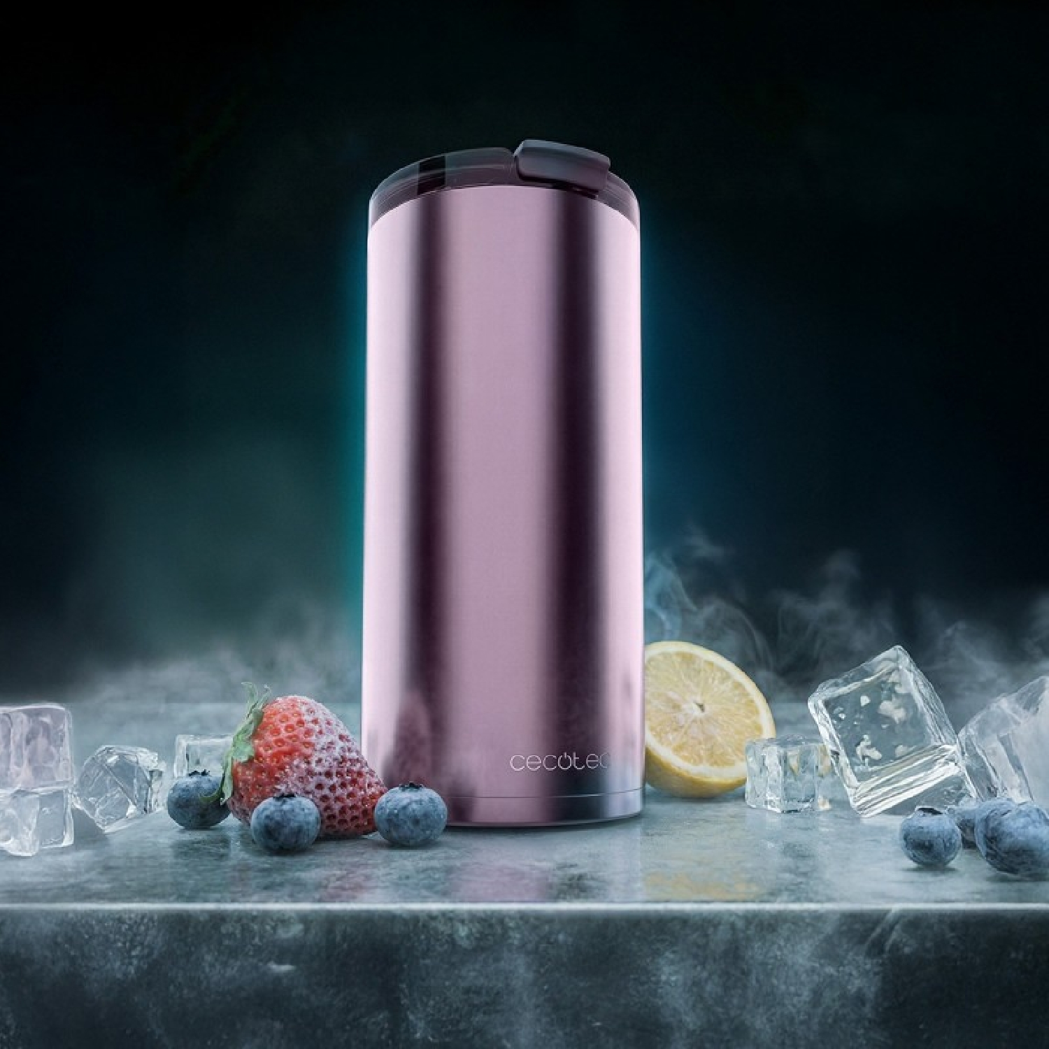 Un vaso metálico rosa con bayas, limón y cubitos de hielo sobre una superficie oscura.