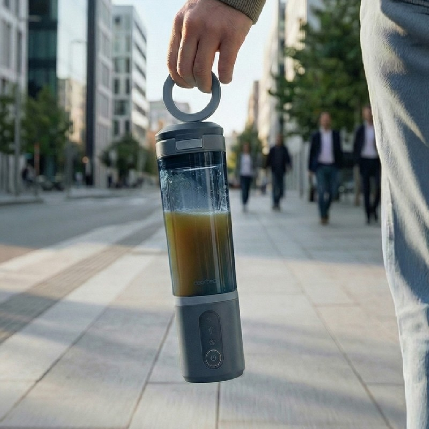 Una mano tiene un frullatore portatile con succo giallo su uno sfondo cittadino.