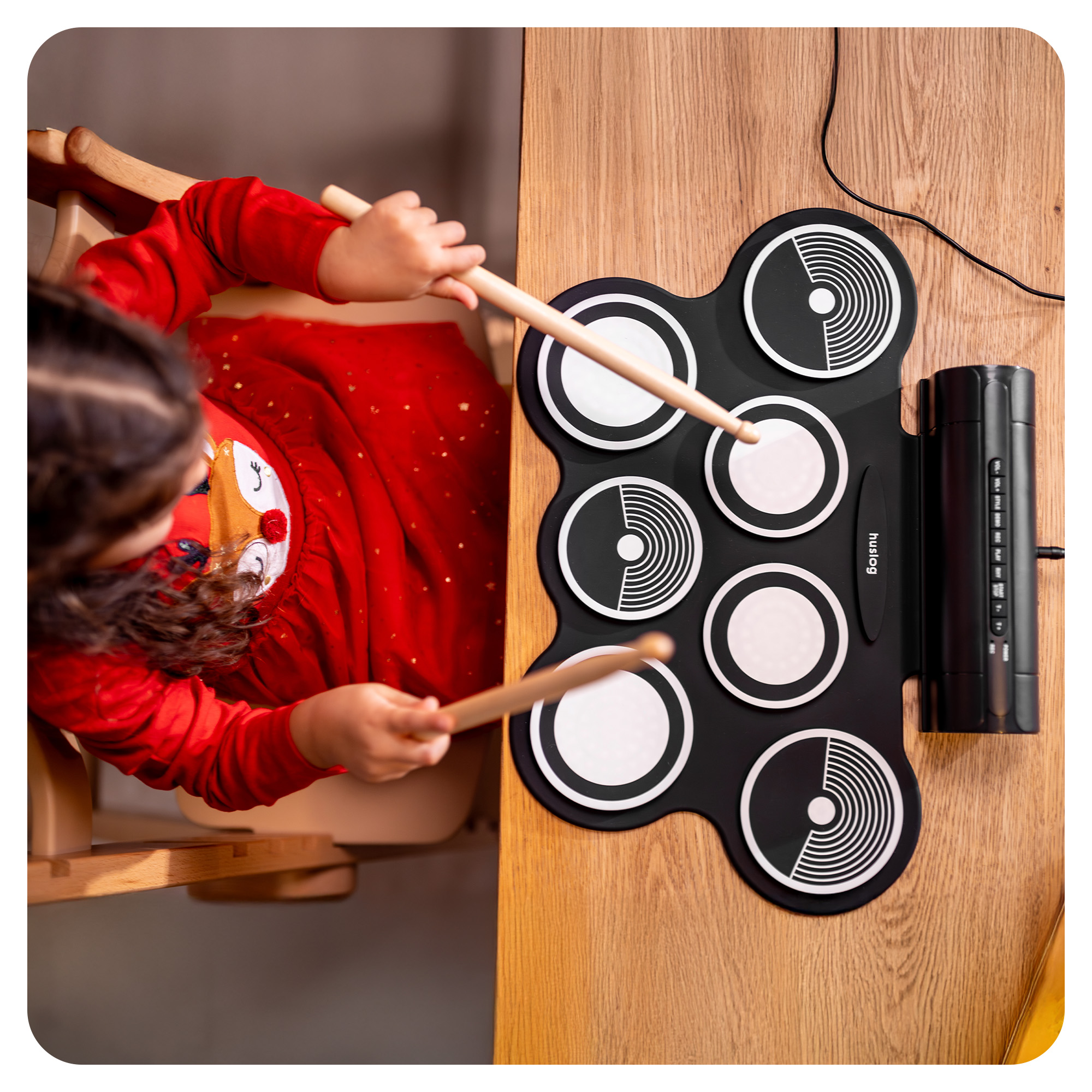 Dziecko w czerwonej sukience gra na cyfrowej macie perkusyjnej pałeczkami.