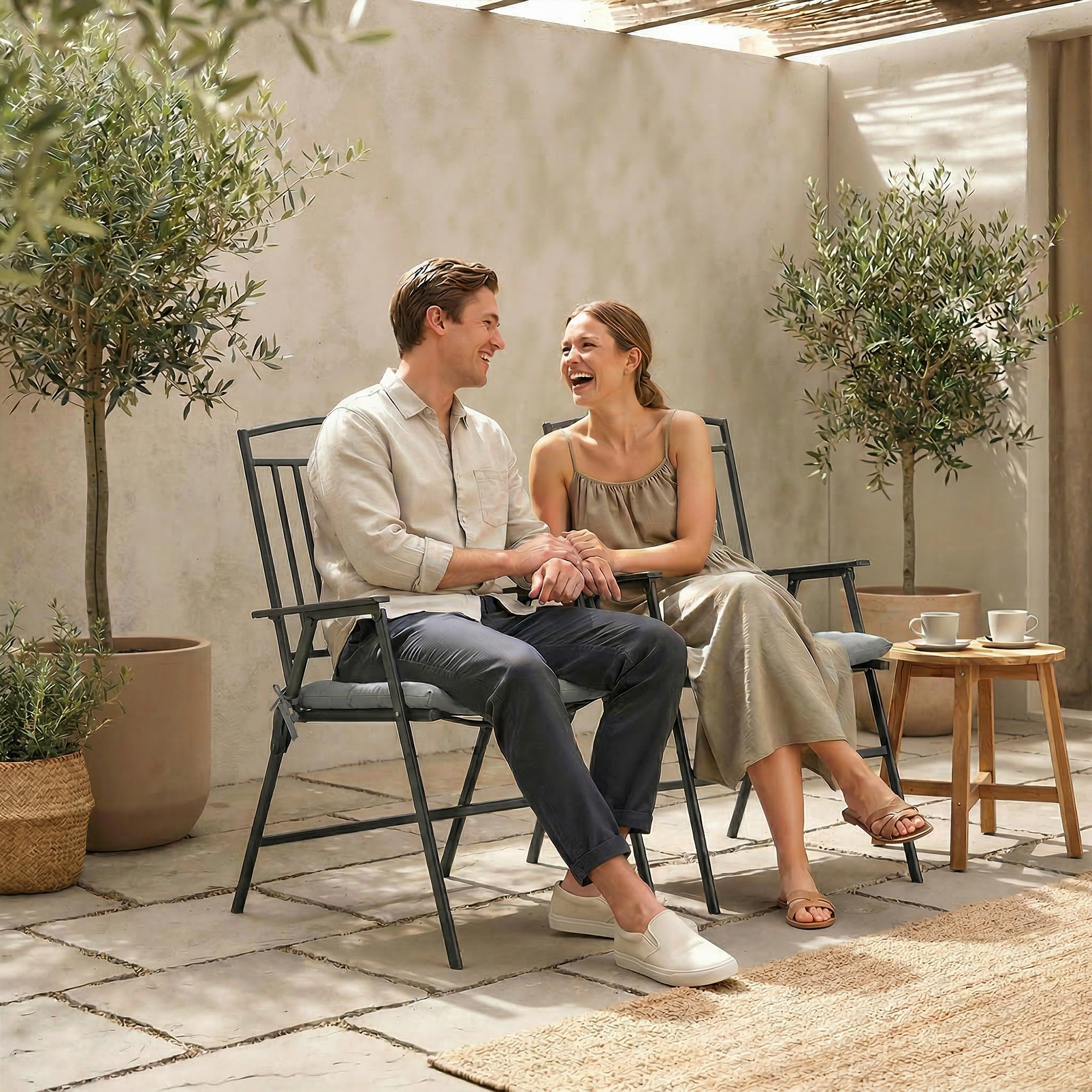 Una pareja se sienta en sillas de jardín, riendo y tomados de la mano.