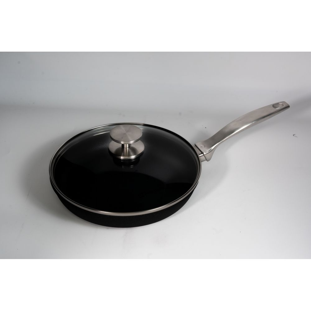 Une poêle noire avec couvercle en verre et manche argenté sur fond gris.