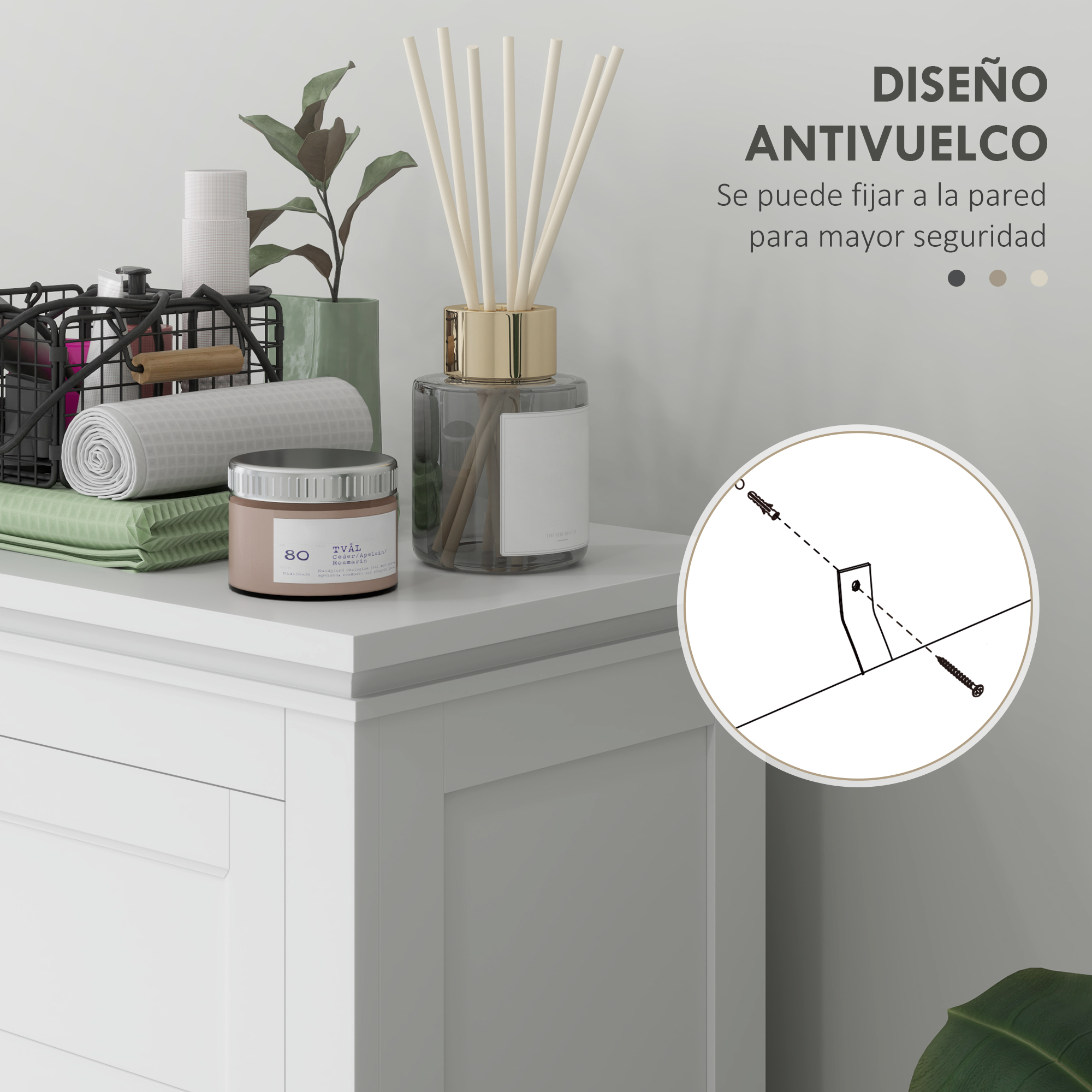 Un difusor, vela y cesta de toallas sobre un mueble blanco. Detalle antivuelco.