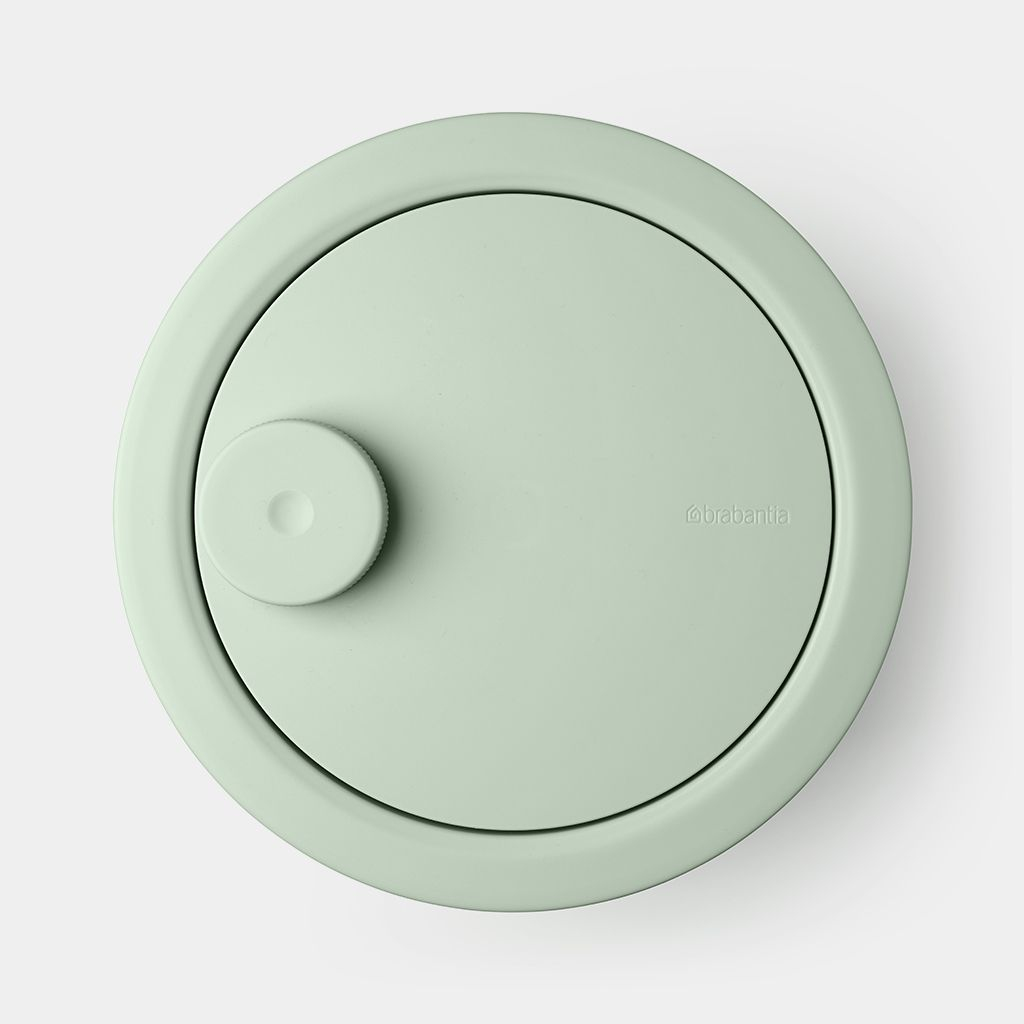 Un coperchio rotondo verde chiaro con una piccola manopola a sinistra.