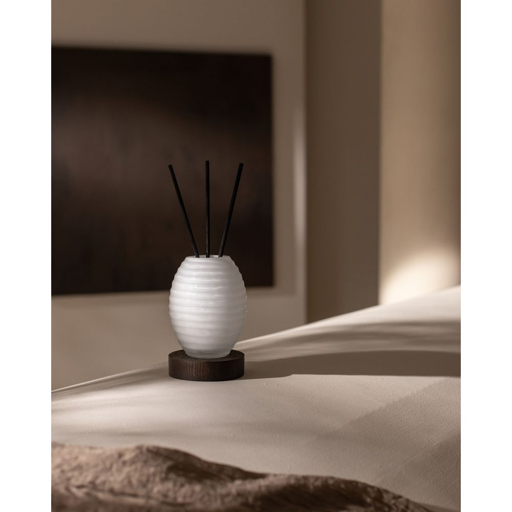 Un diffusore bianco con bastoncini neri poggia su una base di legno scuro.