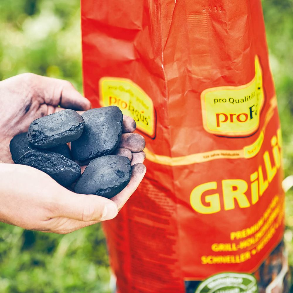 Hände halten Holzkohle vor einer roten Tüte mit der Aufschrift „Grilli“.