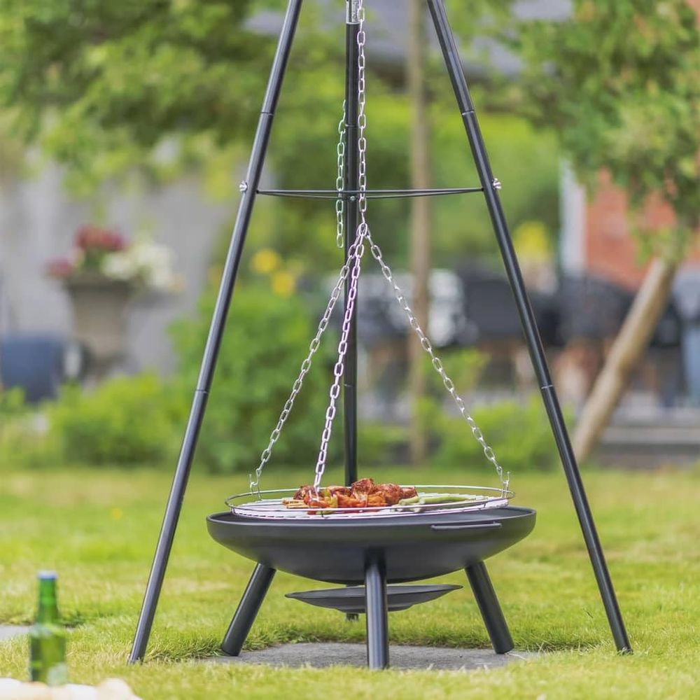 Una griglia a treppiede con carne che cuoce sulla brace in un giardino.