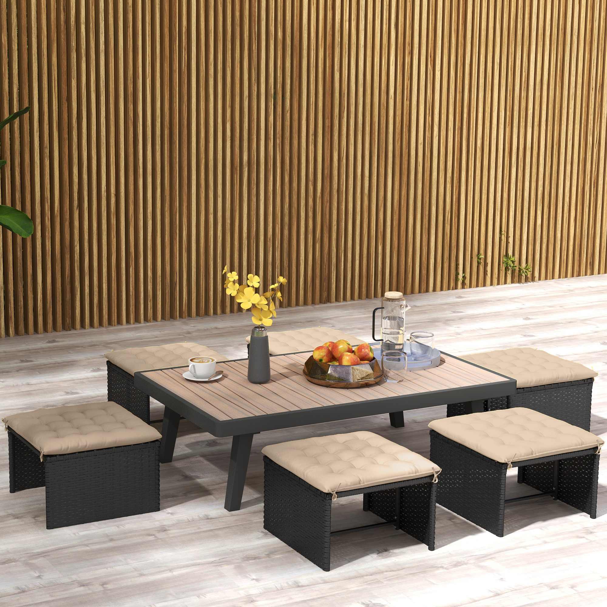 Una mesa de jardín con taburetes, flores y café frente a una pared de madera.