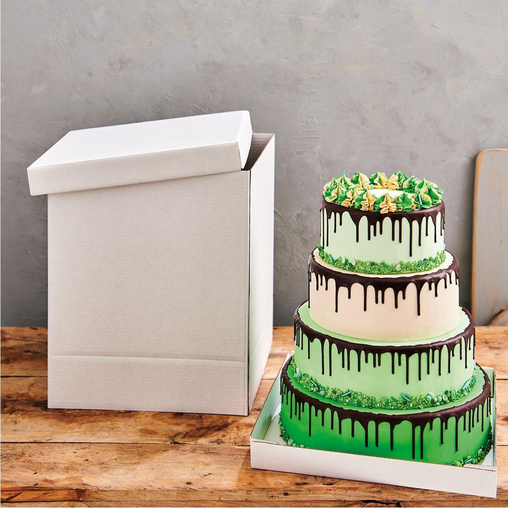 Eine mehrstöckige Torte mit grüner Glasur und Schokoladentropfen steht neben einer offenen weißen Box.