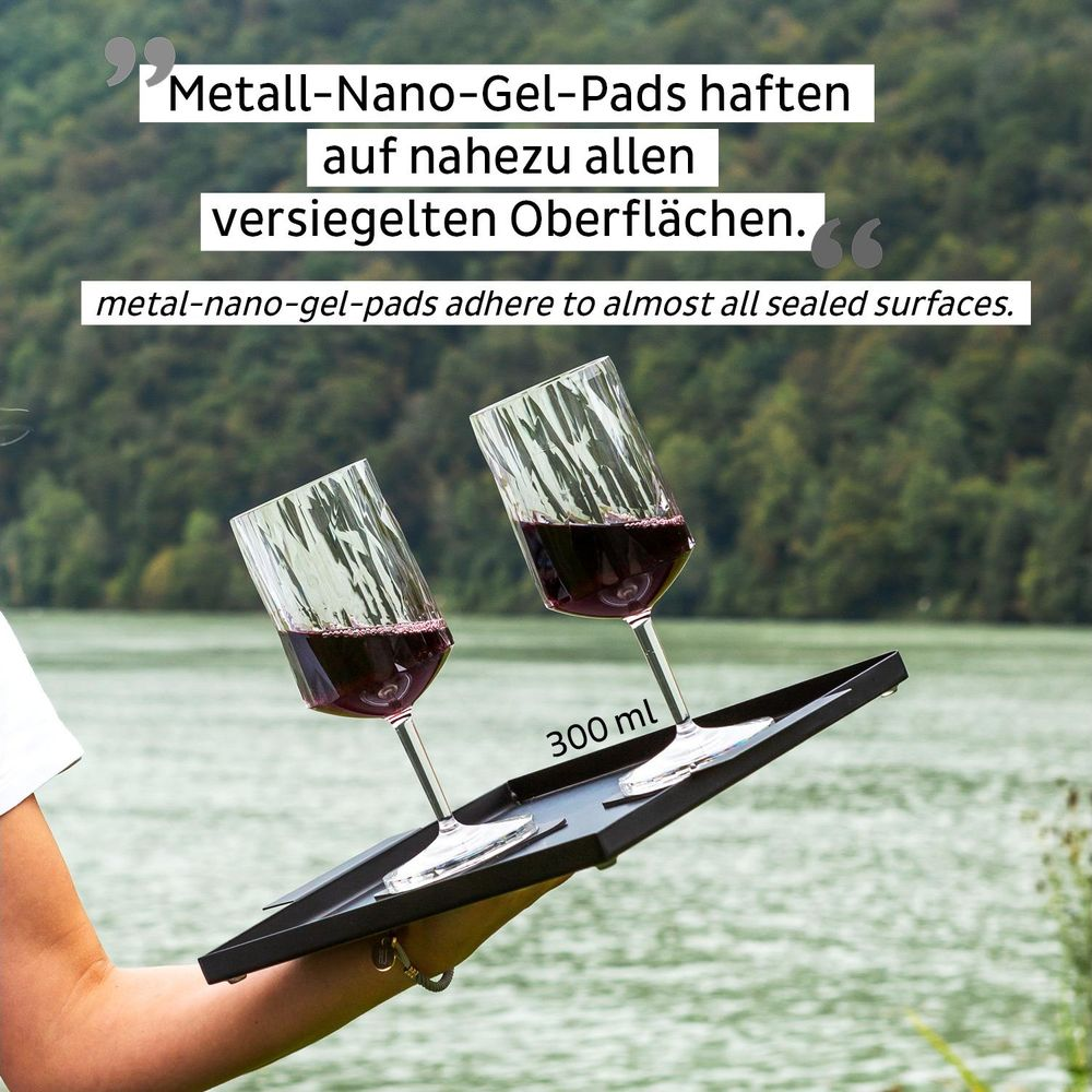 Deux verres à vin avec du vin rouge sur un plateau noir. Un lac en arrière-plan.