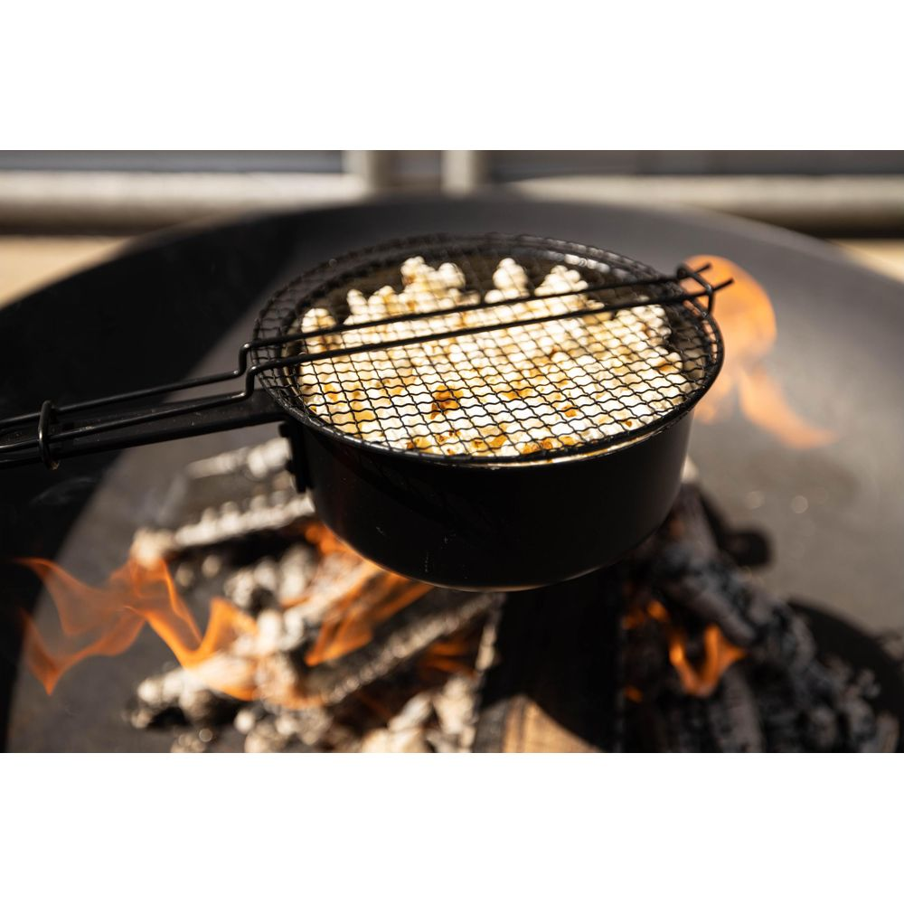 Popcorn dans une marmite noire avec couvercle cuisant sur un brasero avec des flammes.