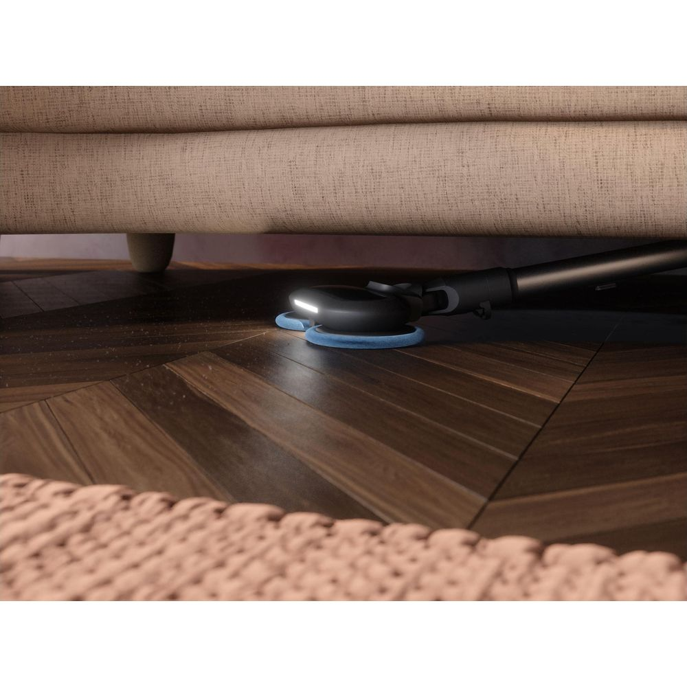Ein Staubsaugerkopf mit LED-Licht reinigt unter einem Sofa auf einem Holzboden.