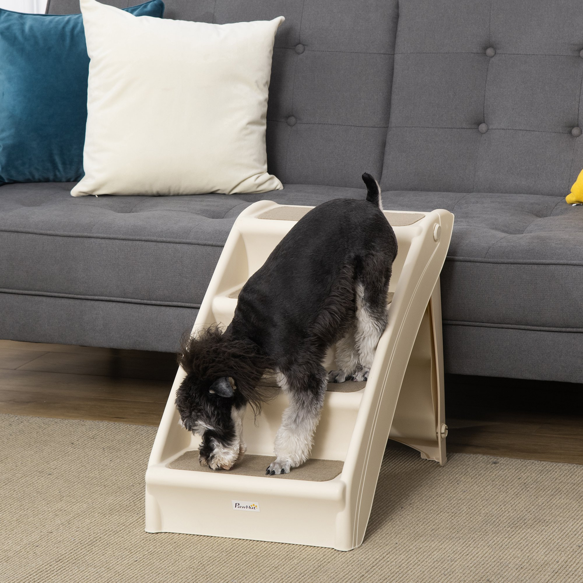 Un perro blanco y negro sube una escalera beige para mascotas junto a un sofá gris.