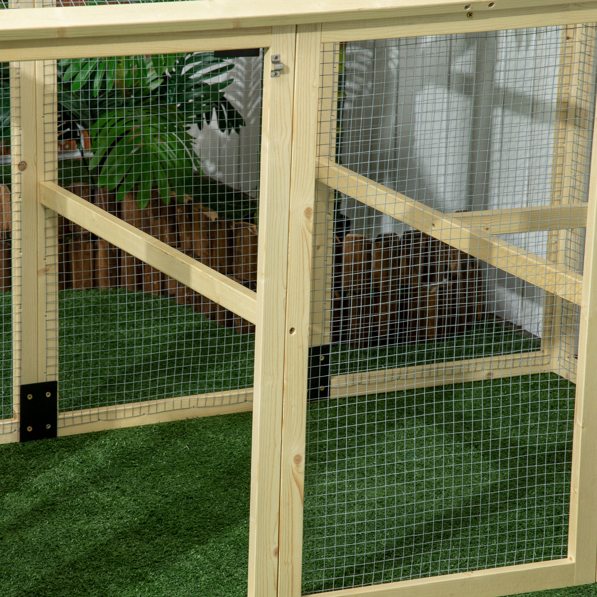 Una jaula de madera con puertas de malla y suelo de césped artificial. Se ven hojas verdes.
