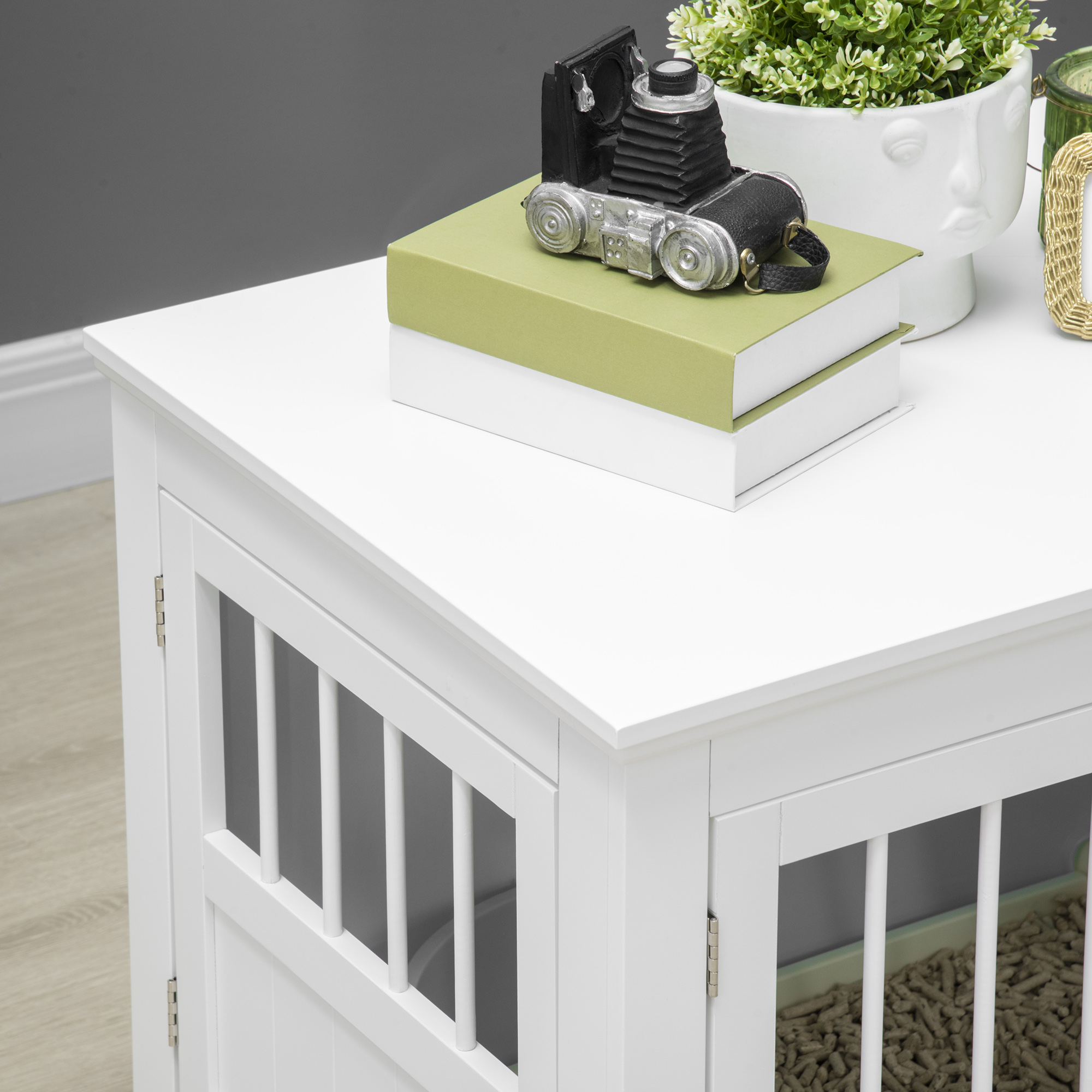 Un mueble blanco para gatos con barrotes y una bandeja con arena para gatos.