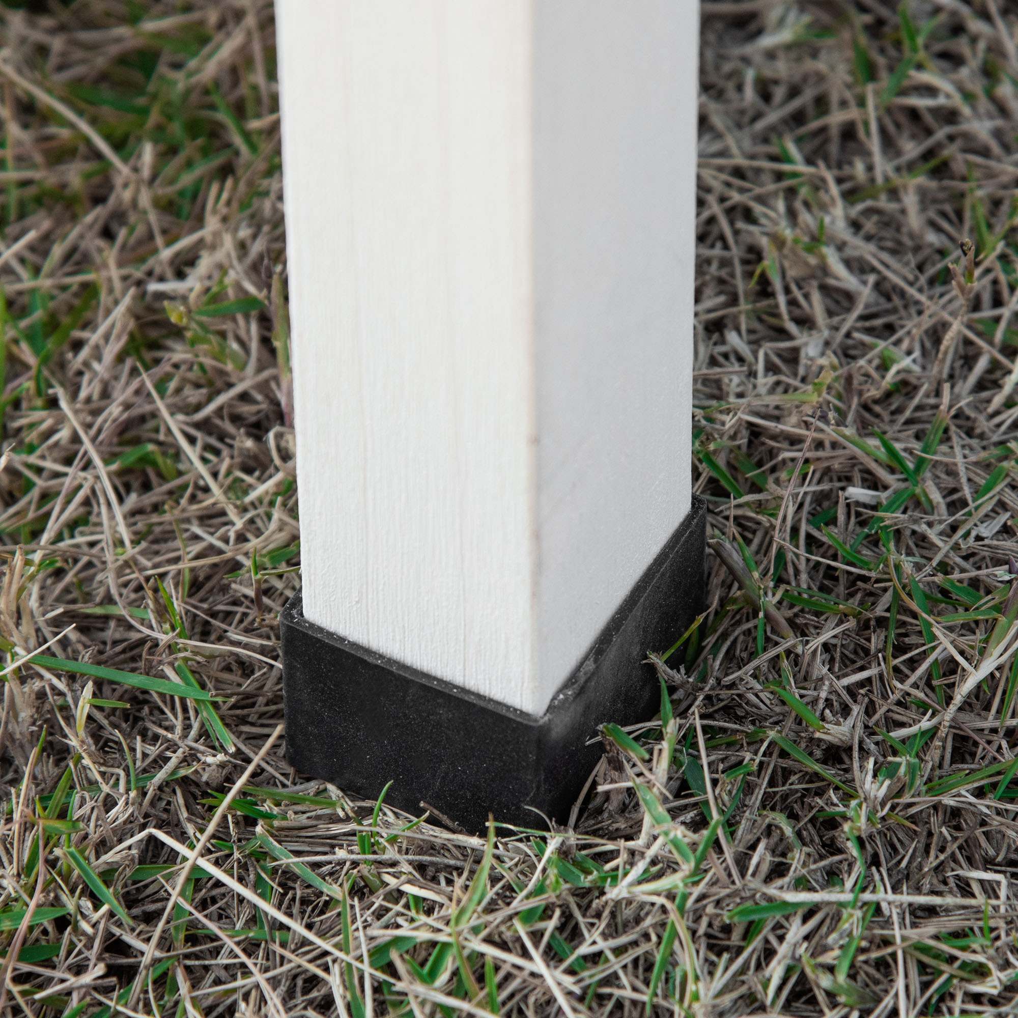 Un poste de madera clara con tapa negra se alza sobre hierba seca.