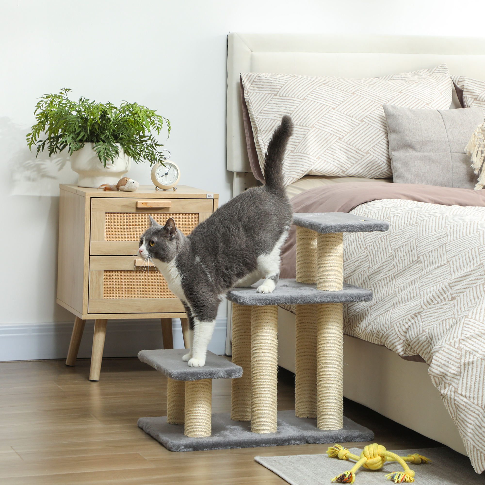 Un gato trepa a un árbol para gatos en un dormitorio junto a una cama.