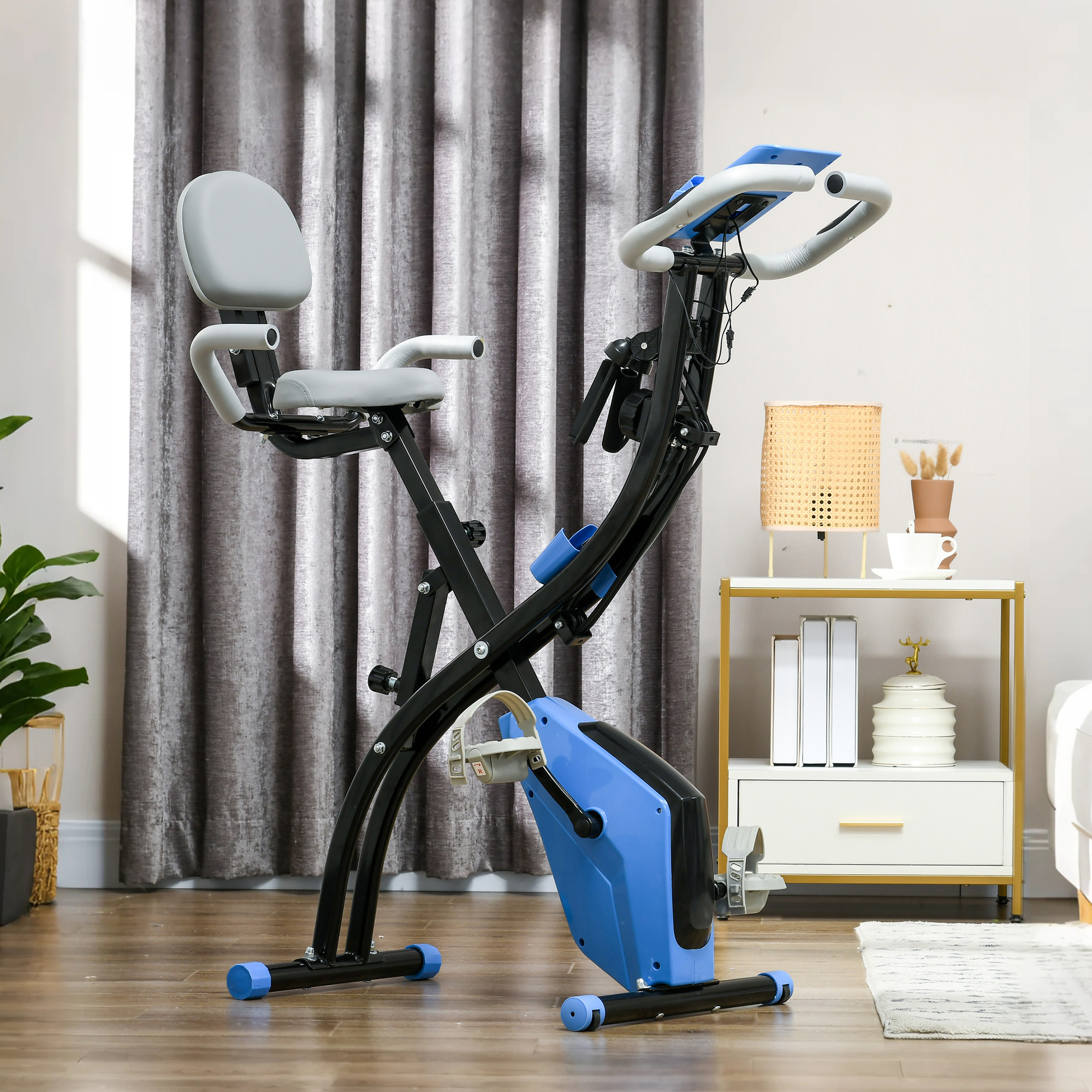Una bicicleta estática plegable con asiento gris y detalles azules está sobre un suelo de madera.