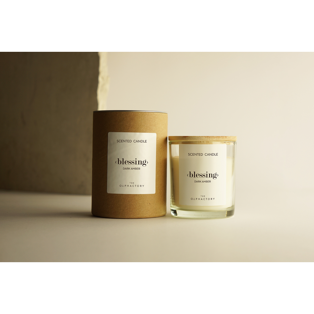Un cilindro marrone e un barattolo di vetro con candele profumate etichettate 'Blessing Dark Amber'.