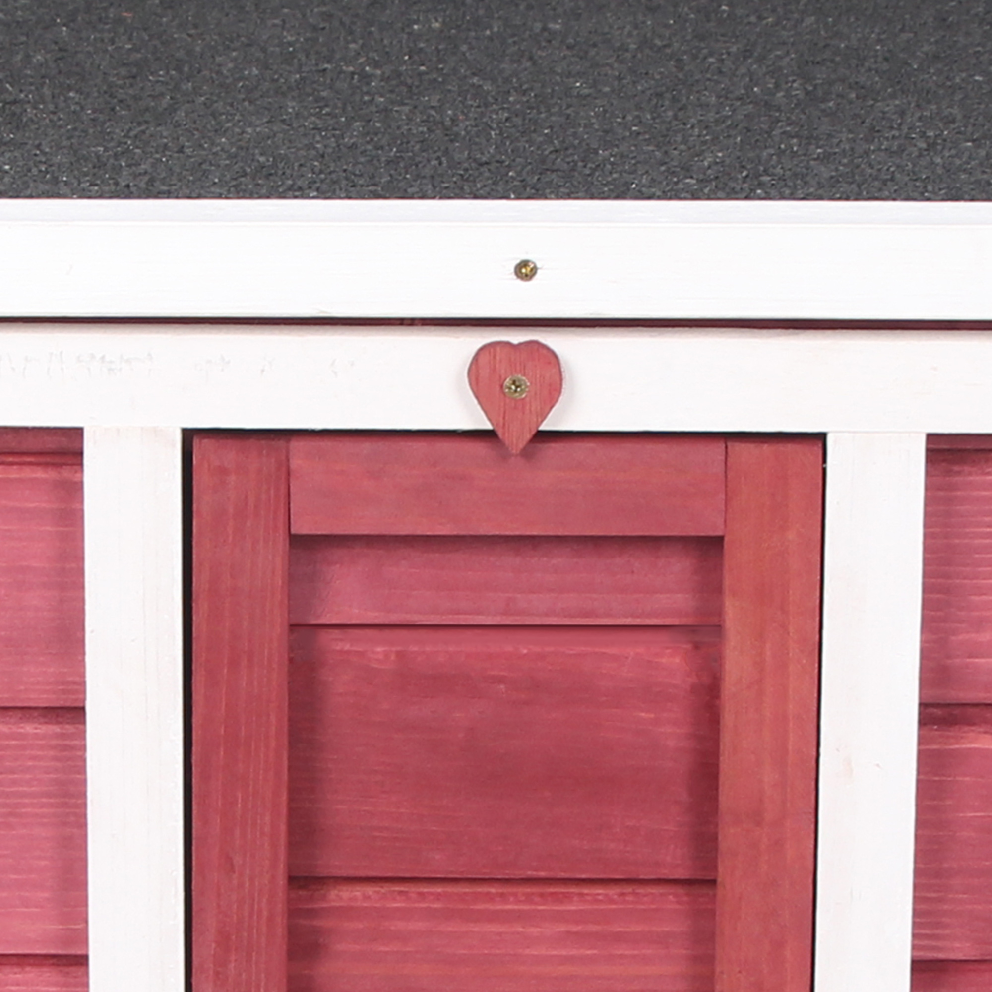 Un detalle de corazón rojo está sujeto a una valla de madera blanca con puerta roja.