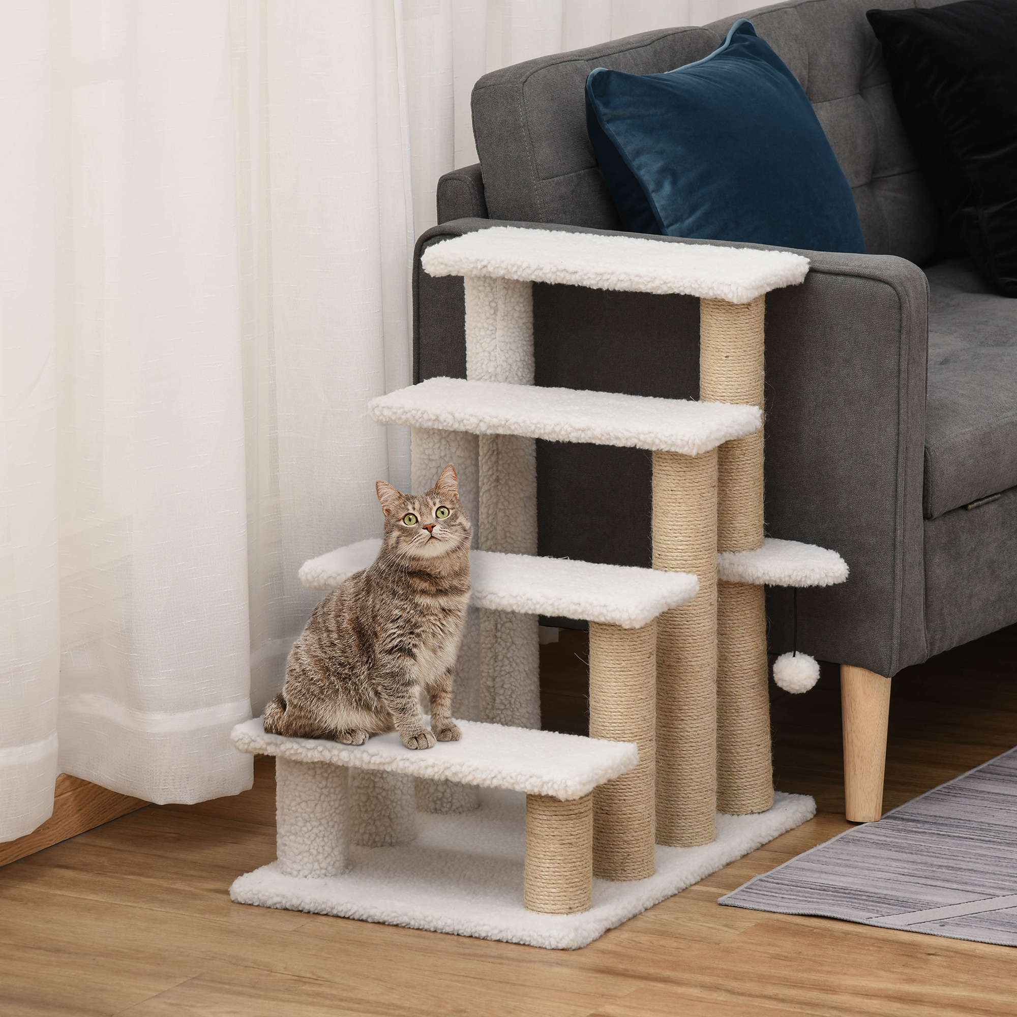 Un gato se sienta en un escalón de árbol para gatos blanco junto a un sofá gris.