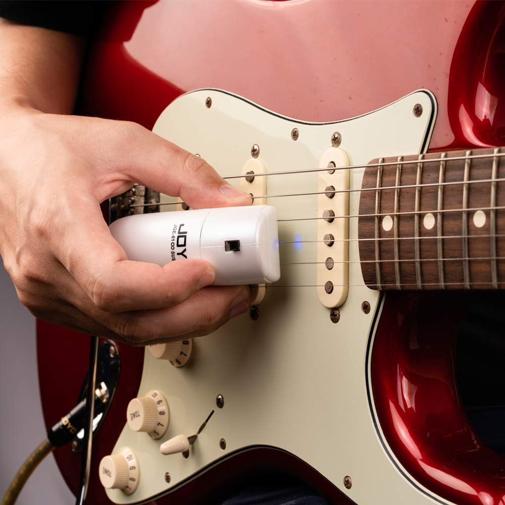 Bir el, beyaz manyetiklere sahip kırmızı bir elektro gitarın üzerinde beyaz bir JOY cihazı tutuyor.