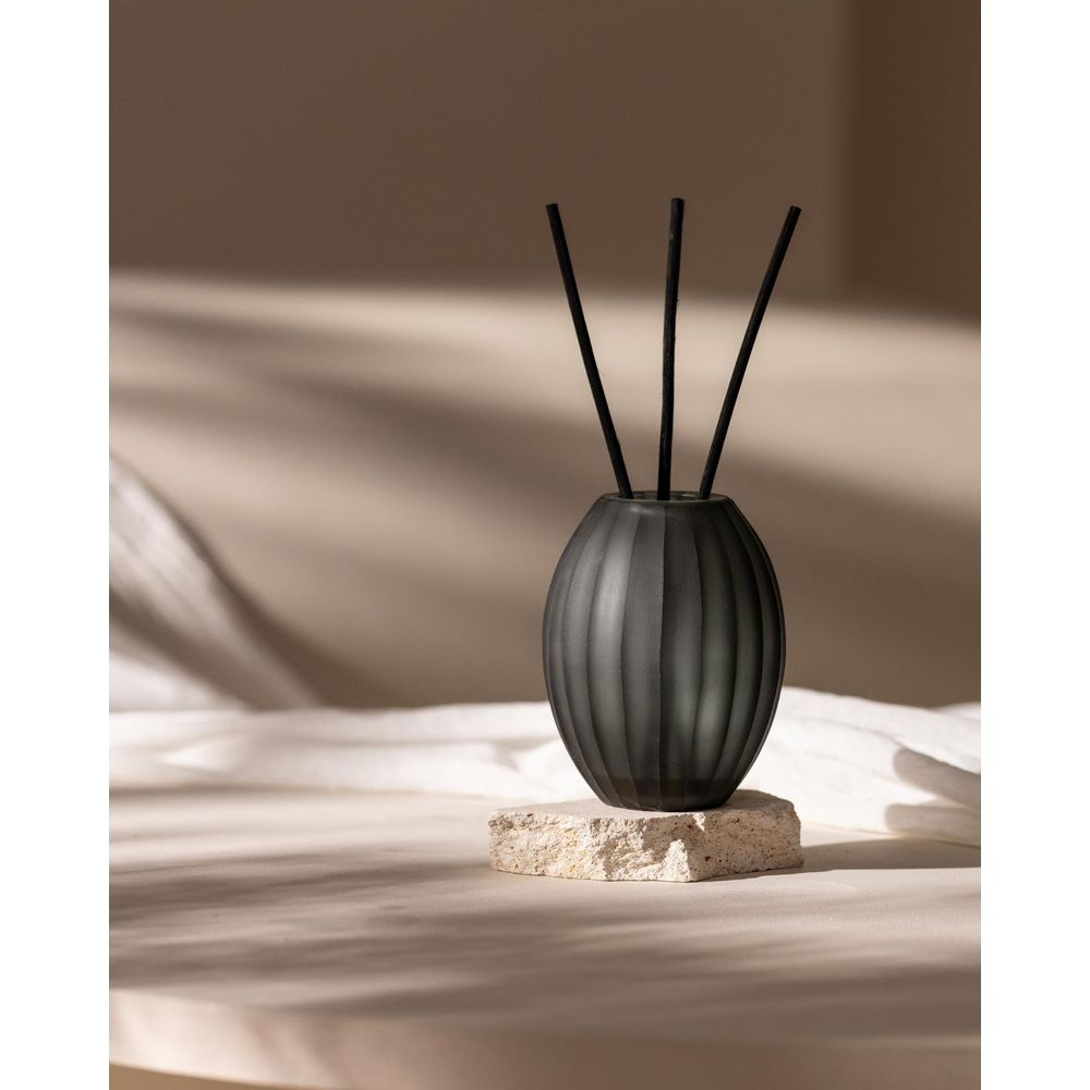 Diffusore nero con tre bastoncini su una pietra, davanti a un tessuto drappeggiato.
