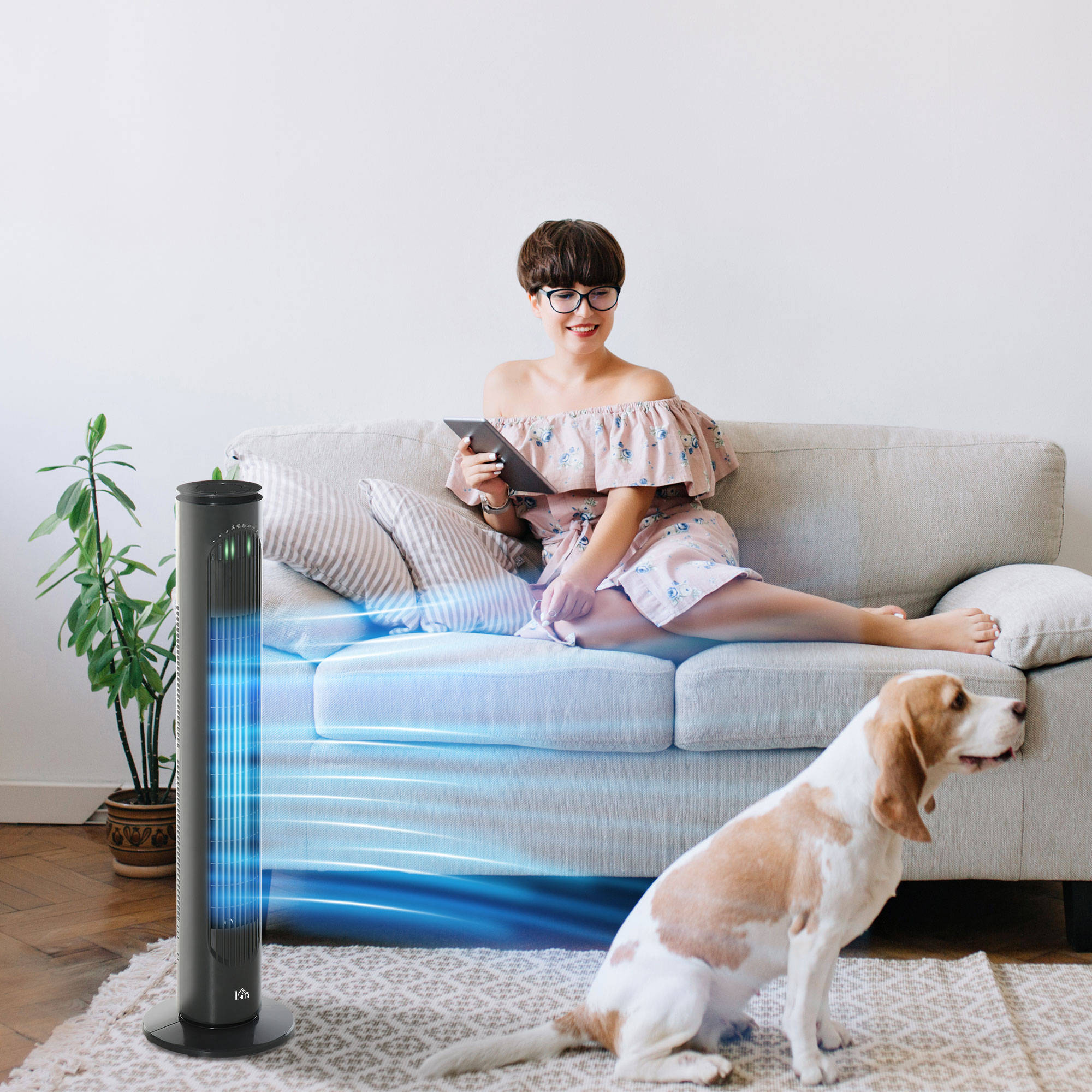 Mujer en sofá con tablet, ventilador de torre soplando aire, perro en alfombra.