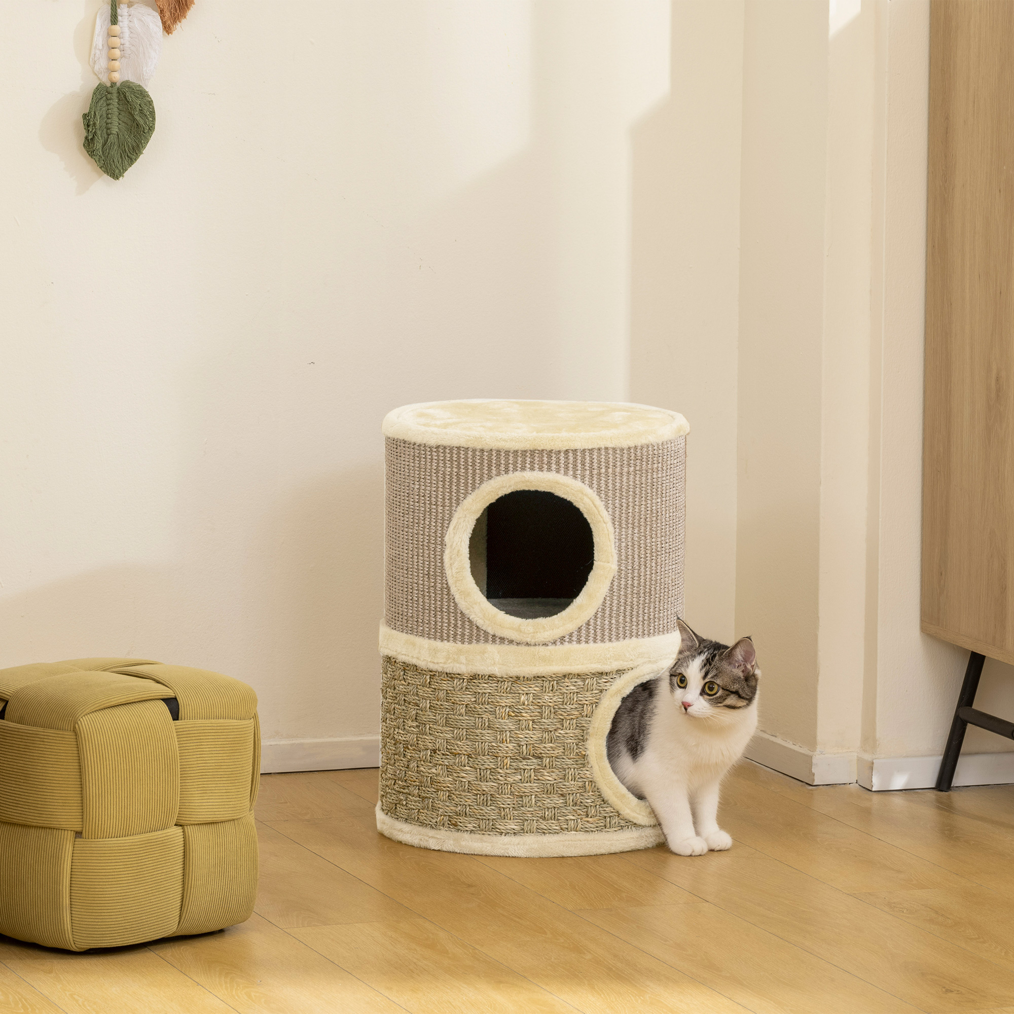 Un gato se sienta junto a un árbol para gatos de dos niveles y un puf amarillo.