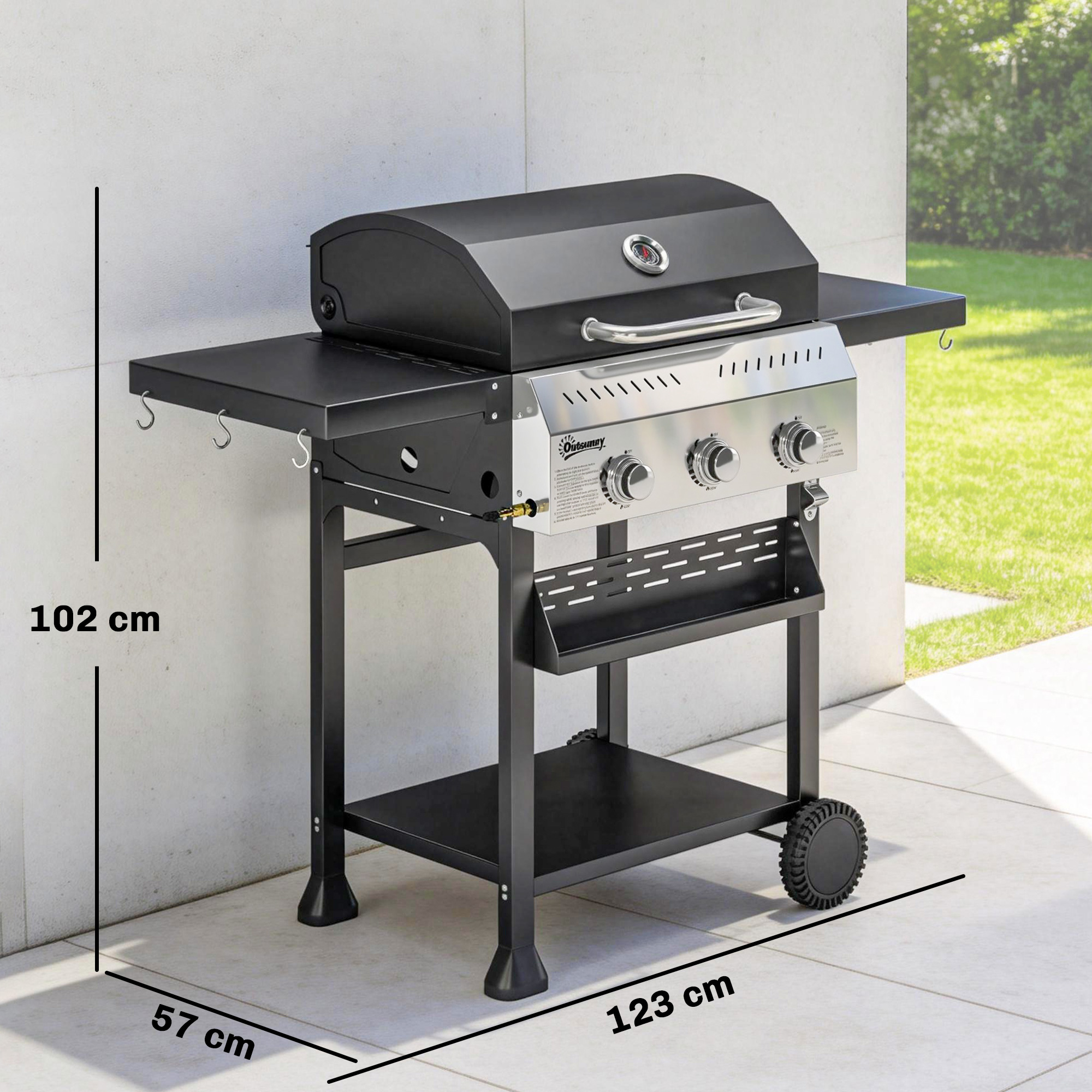 Una parrilla de gas negra con frente plateado está sobre un patio embaldosado.