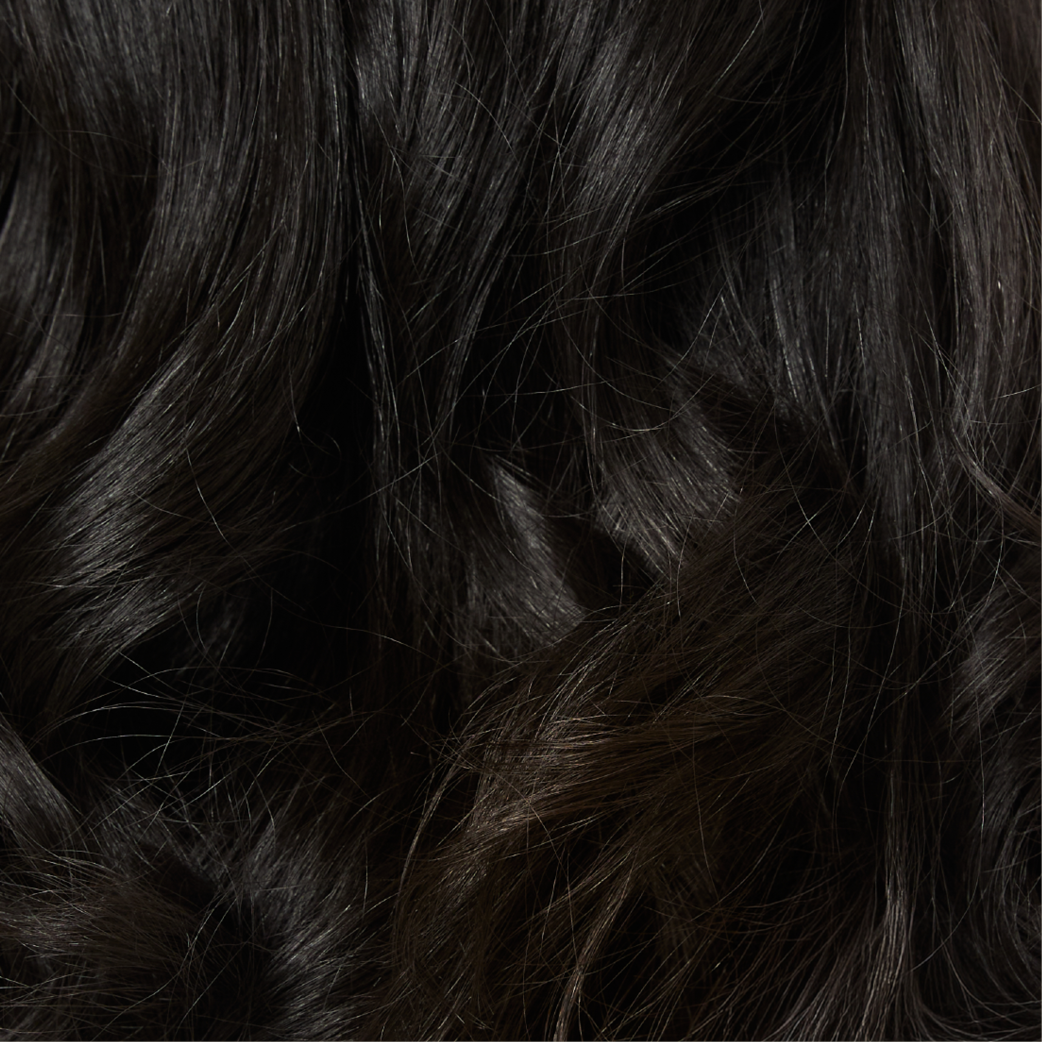 Gros plan de cheveux bruns foncés et ondulés avec des reflets.