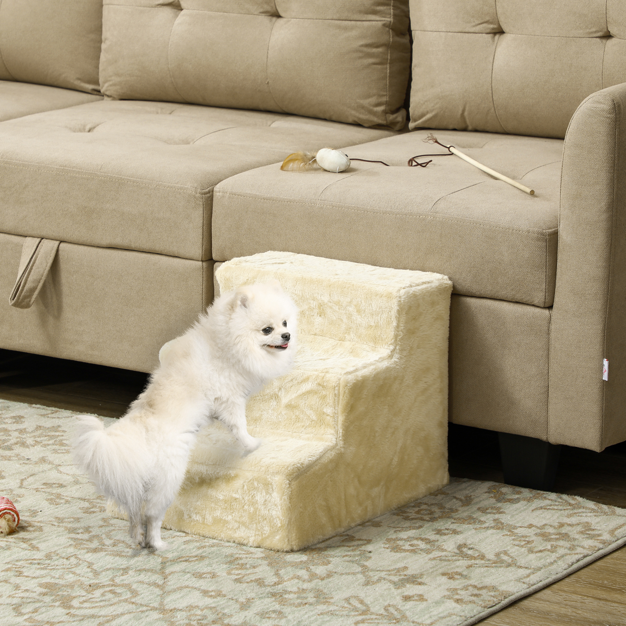Un cachorro Pomerania blanco sube una escalera para perros color crema frente a un sofá.