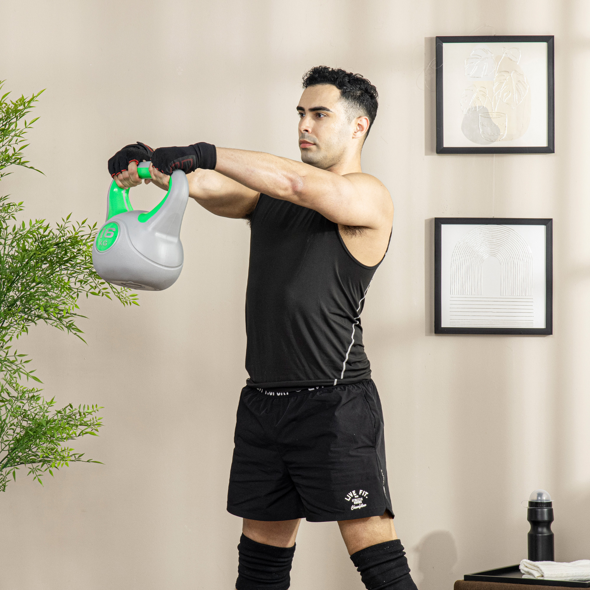Hombre con ropa deportiva negra sosteniendo una pesa rusa gris y verde.