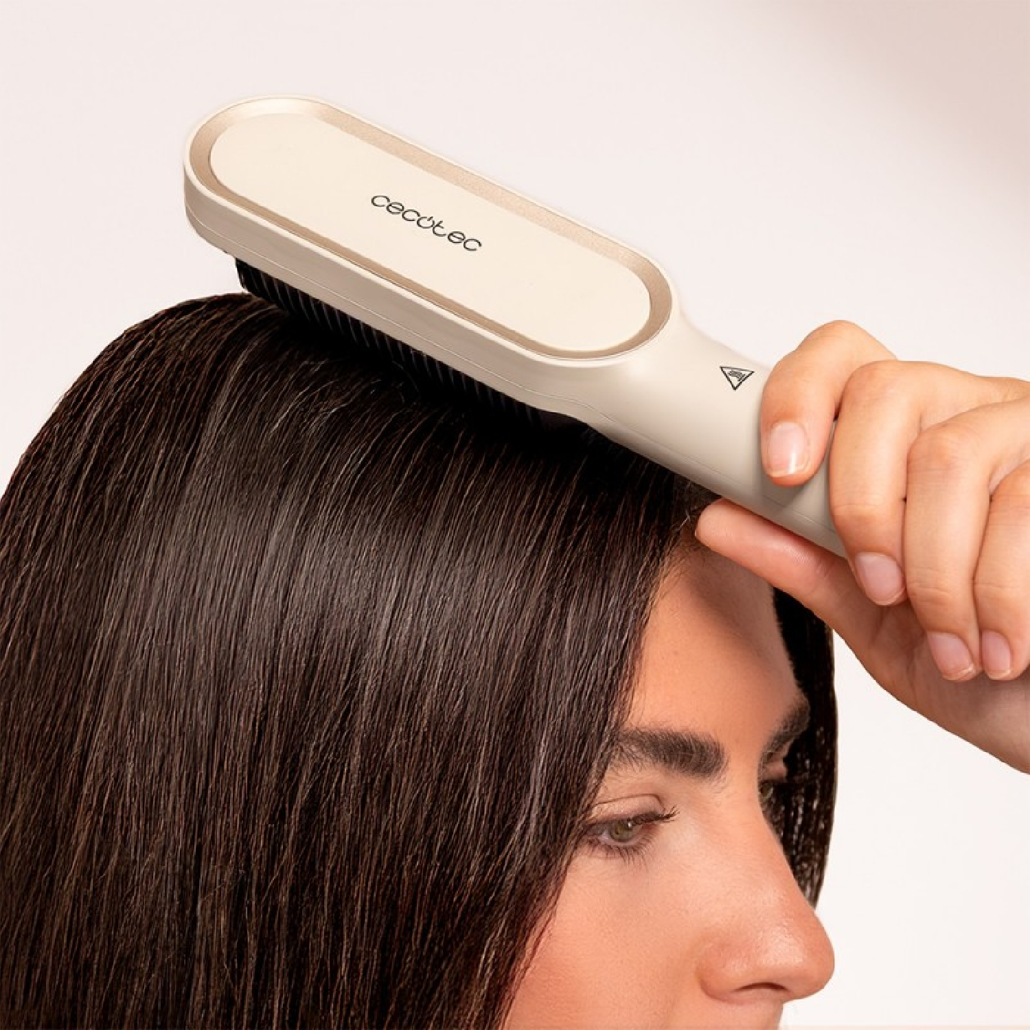 Eine Hand hält eine Cecotec Haarglättungsbürste über dunklem, nassem Haar.
