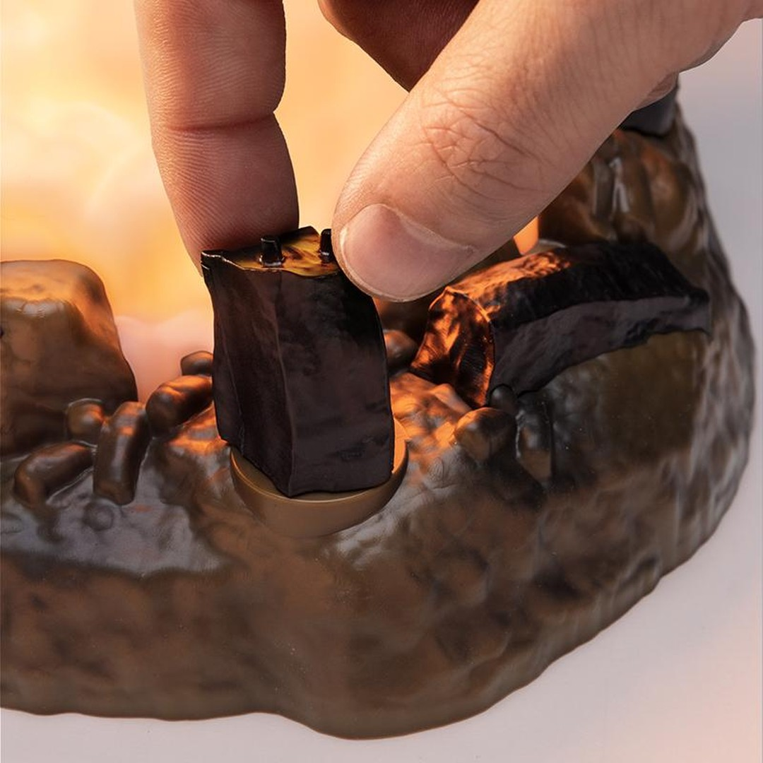 Palec umieszcza ciemny obiekt na brązowej, skalistej strukturze.